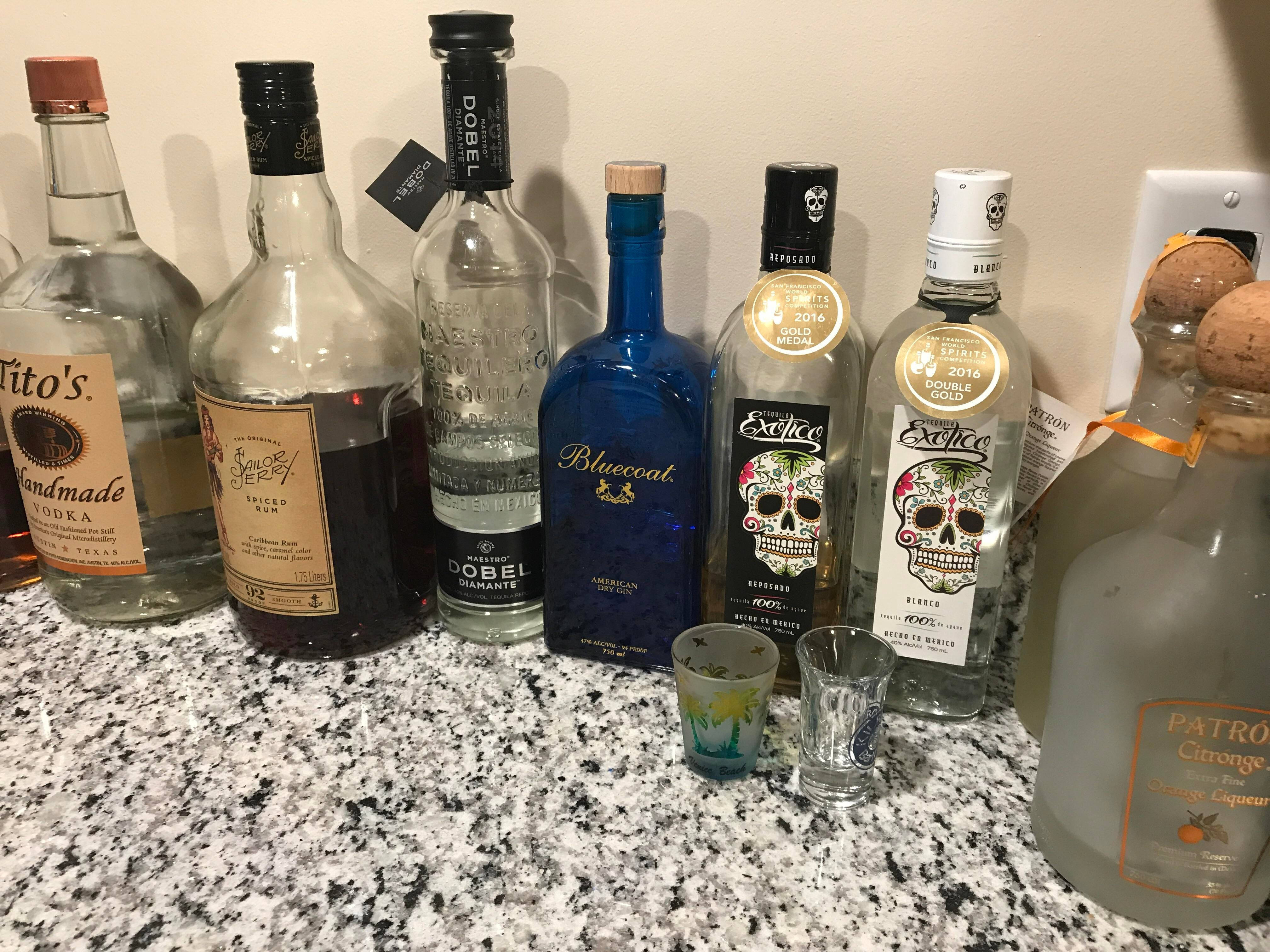bottle 桌布 壁紙 — 一排色彩繽紛的酒瓶和烈酒杯整齊排列在有斑點的花崗岩檯面上。