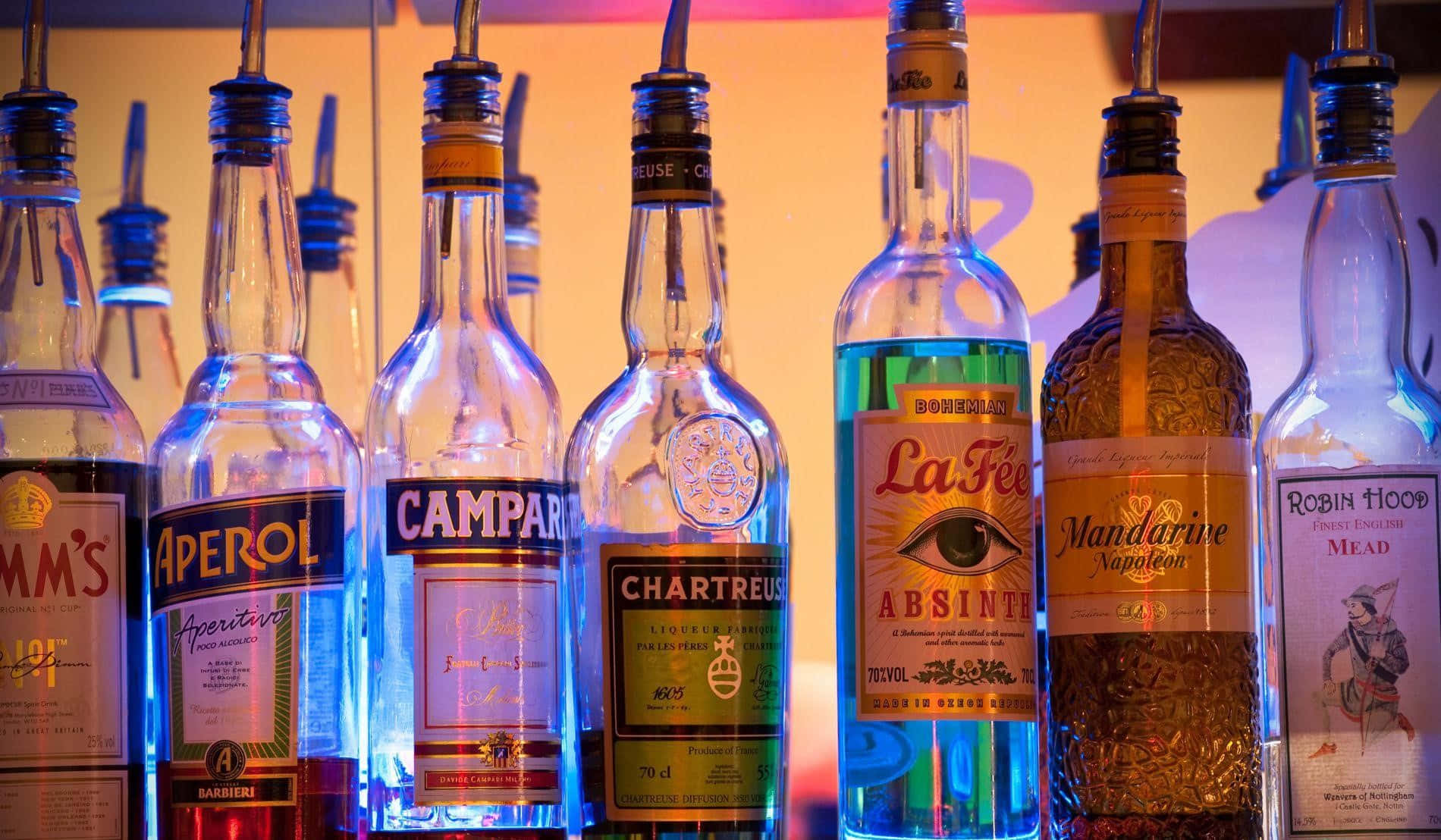 alcohol 桌布 壁紙 — 一排色彩繽紛的酒瓶在溫暖發光的背景下被霓虹燈照亮。
