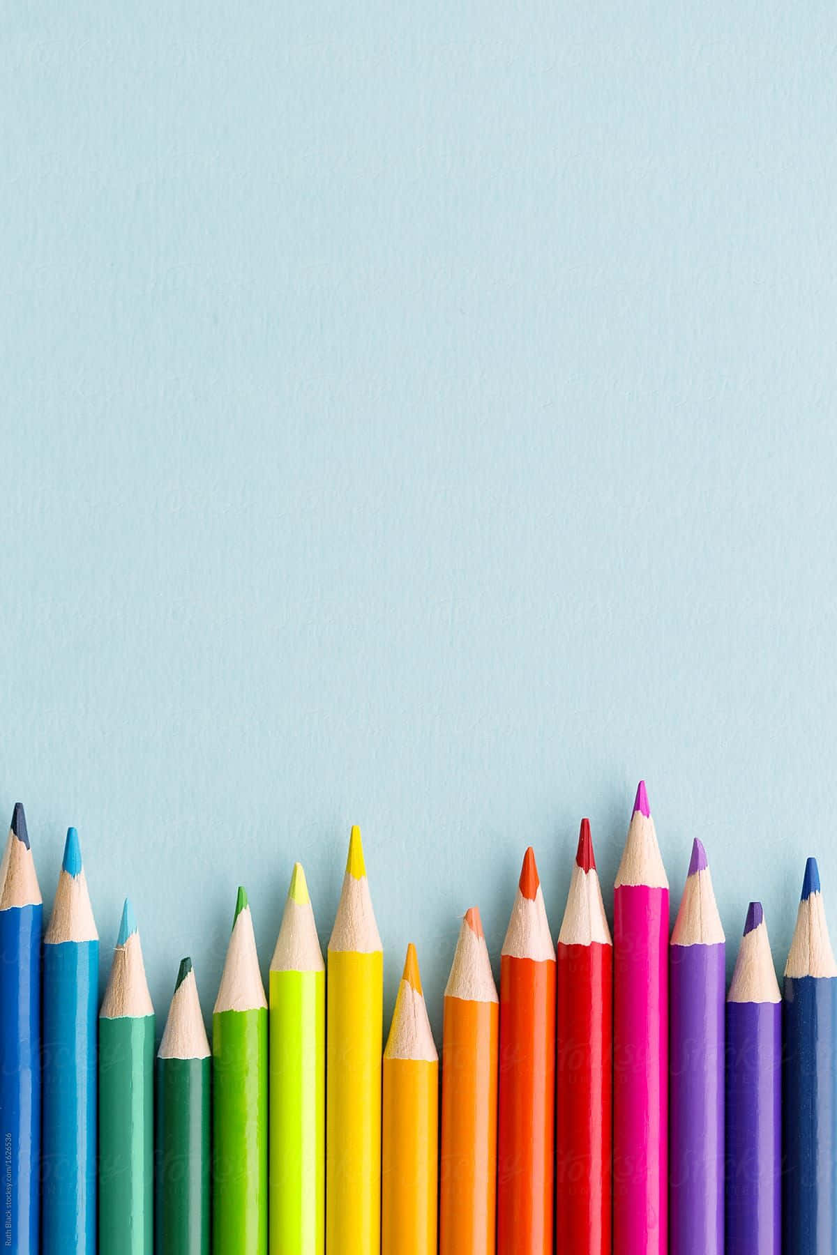 pencil 桌布 壁紙 — 一排色彩鮮豔的削尖彩色鉛筆以彩虹色調排列在底部，背景為柔和的藍色紋理。