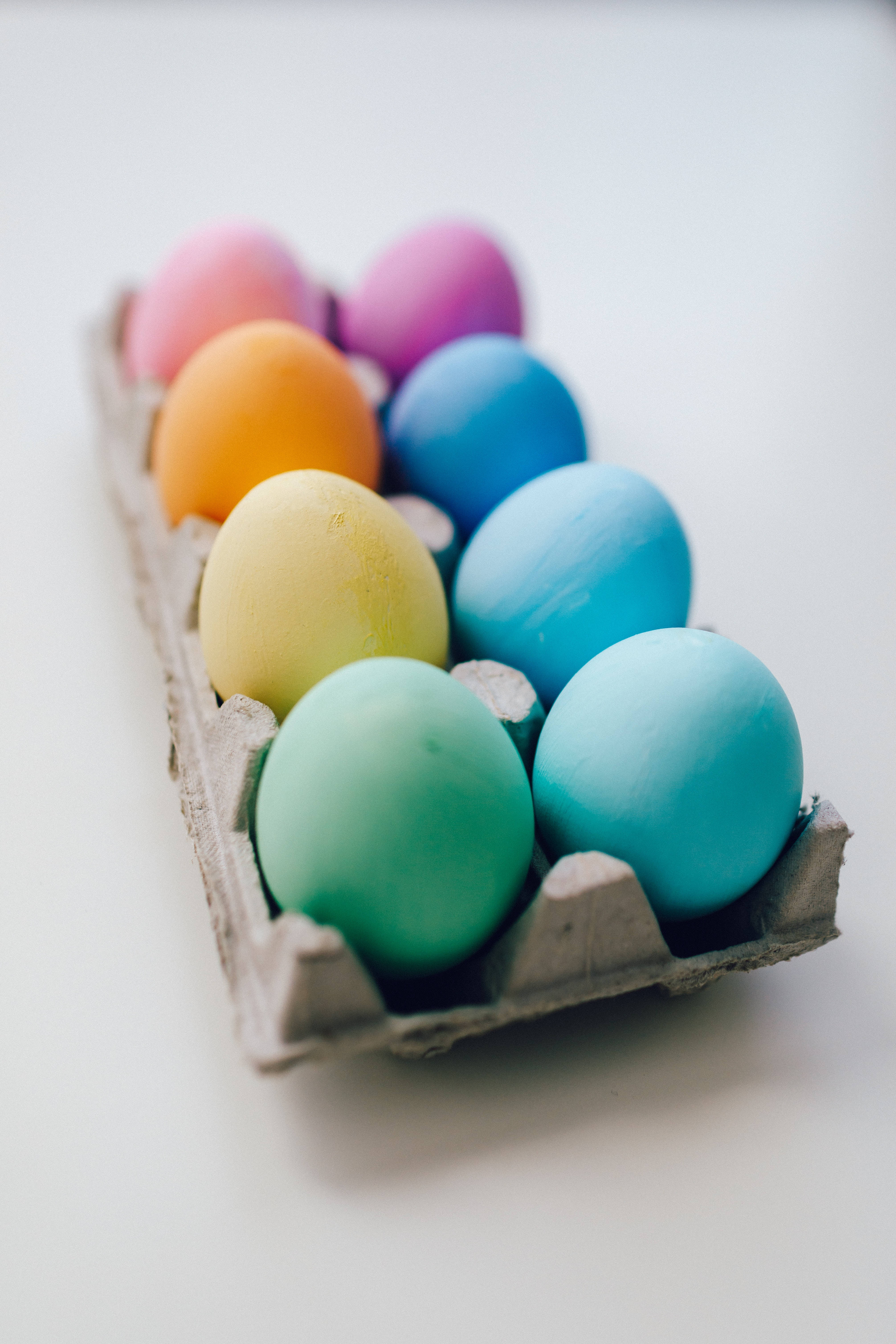 Egg 桌布 壁紙 — 一排色彩鮮豔的雞蛋放在紙板托盤中，以彩虹漸層排列在柔和的白色背景上。