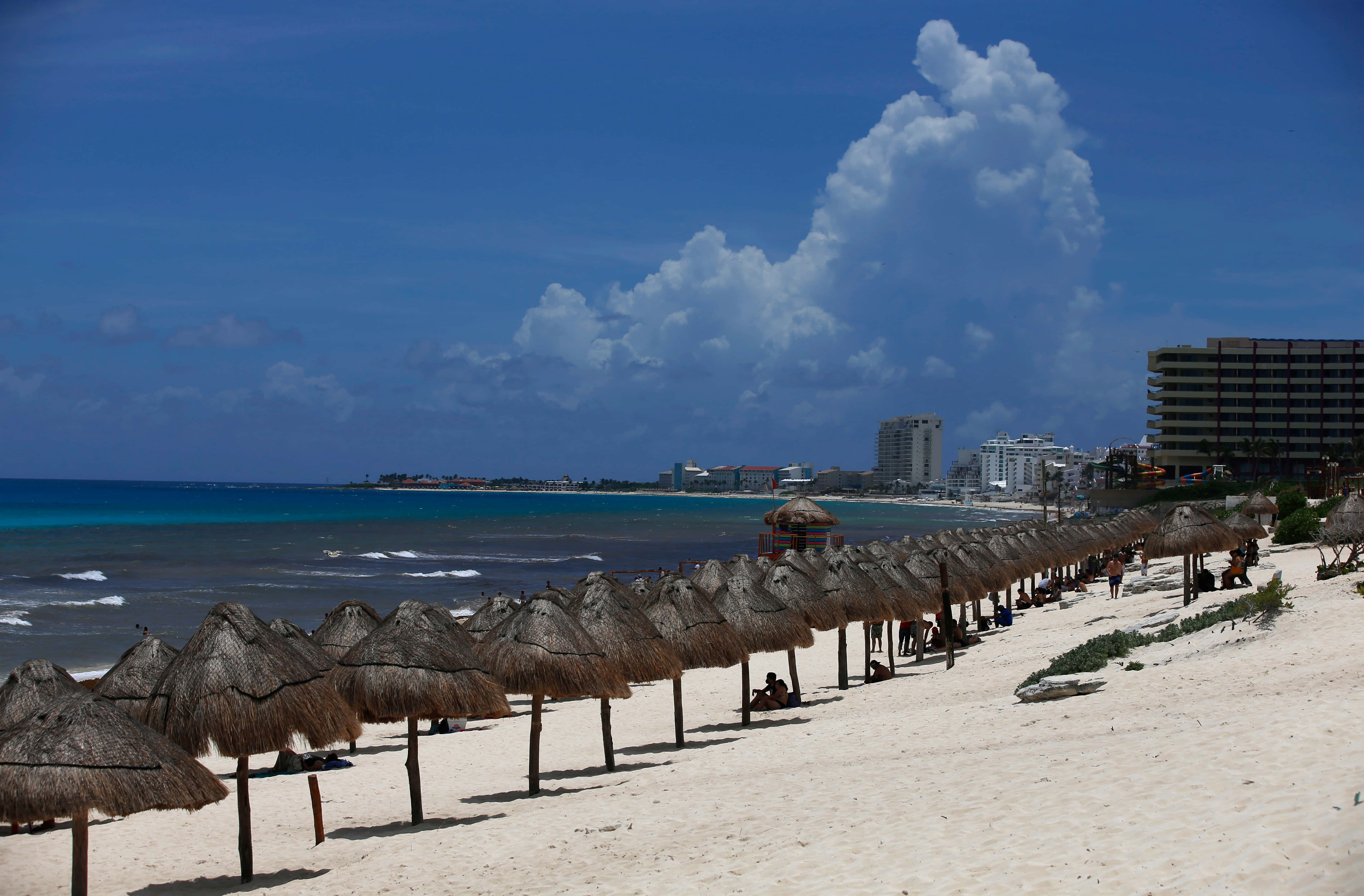 Mexican Beach 桌布 壁紙 — 一排茅草傘沿著白色沙灘排列，在明亮的藍天下，有戲劇性的雲朵和碧綠的海浪。