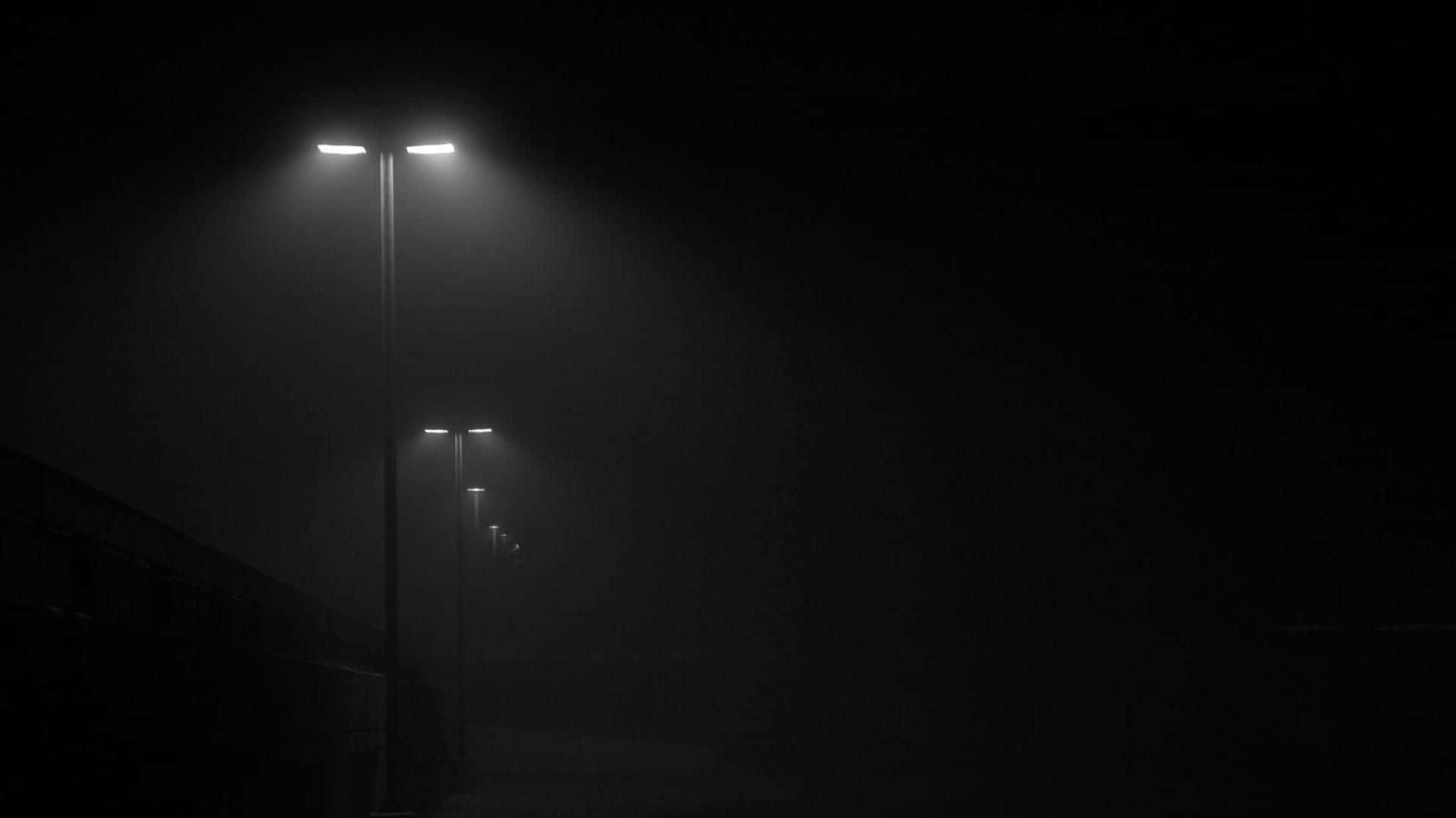 夜空 桌布 壁紙 — 一排街燈穿透濃霧，在寂靜的城市夜晚中，將刺眼的白色光束投射進黑暗。