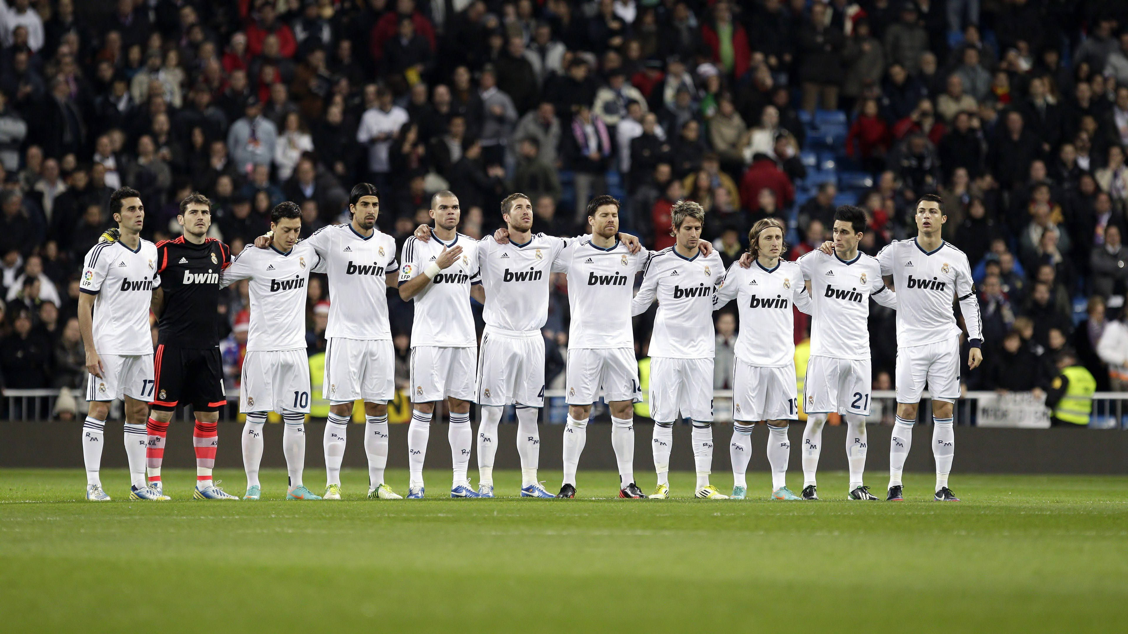 Real Madrid 4K 桌布 壁紙 — 一排身穿白色球衣的皇家馬德里足球員莊嚴地站在綠色球場上，身後是座無虛席的體育場。