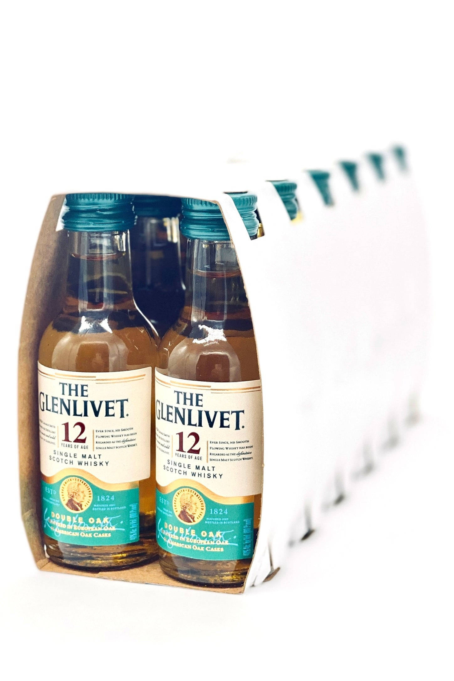 drinks 桌布 壁紙 — 一排迷你 The Glenlivet 12 年威士忌酒瓶放在紙板托架上，背景為純白色。