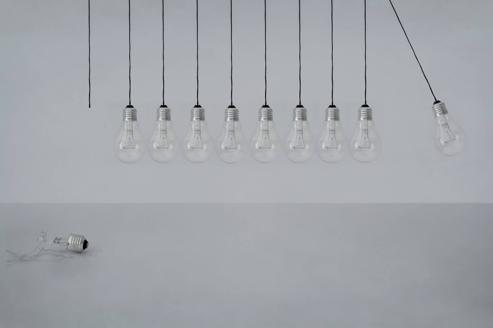 Light 桌布 壁紙 — 一排透明燈泡用黑色電線掛在素色灰色牆上，其中一個燈泡破碎在地上。
