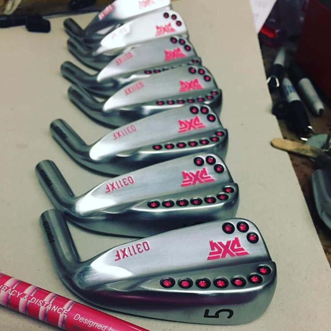 Golf Club 桌布 壁紙 — 一排閃亮的銀色 PXG 高爾夫鐵桿，帶有紅色點綴，整齊地排列在工作台上。