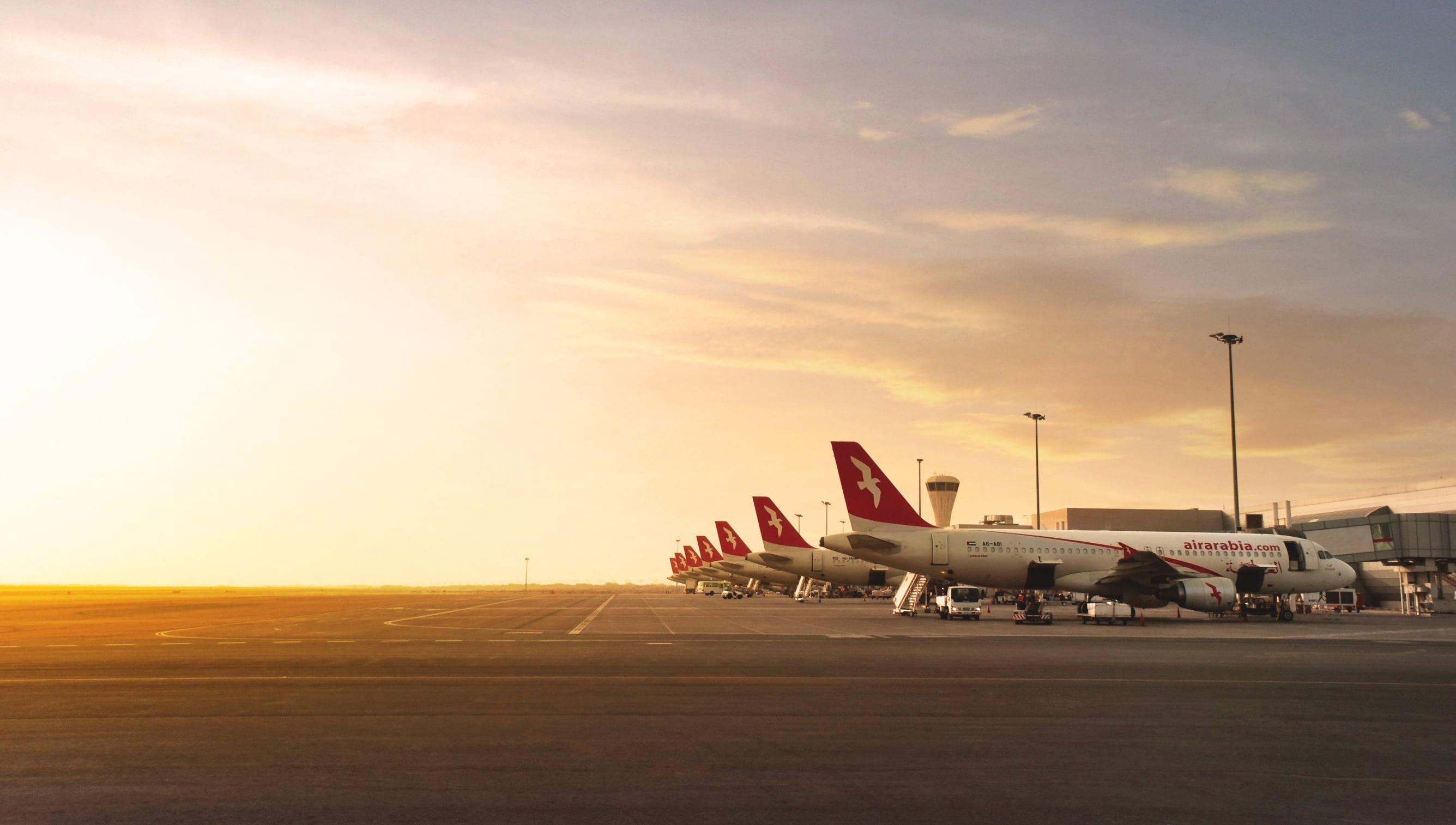 Airport 桌布 壁紙 — 一排阿拉伯航空飛機停泊在機場航廈，沐浴在夕陽溫暖的金色光芒中。