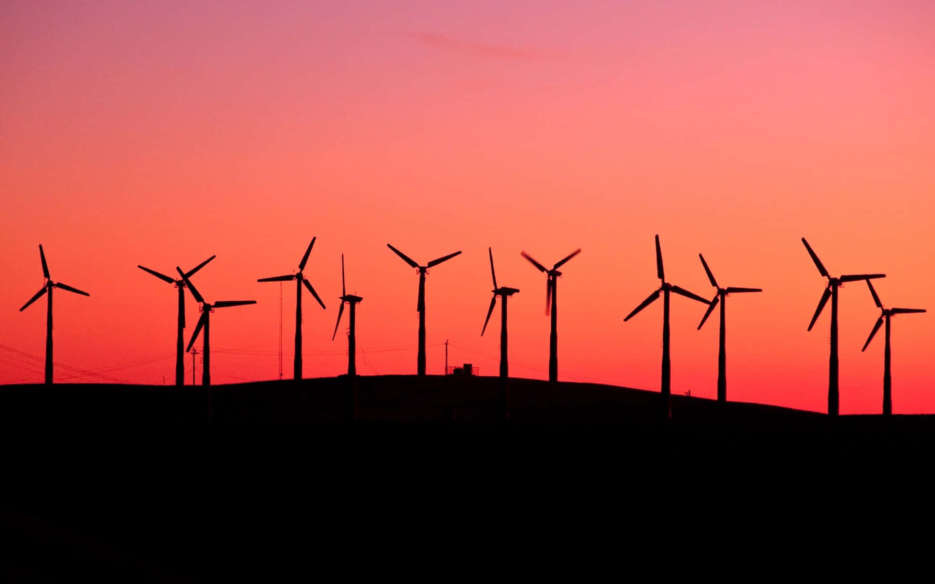 Wind 桌布 壁紙 — 一排風力渦輪機的剪影矗立在火紅的夕陽天空前，散發著橙色和粉紅色的光芒。