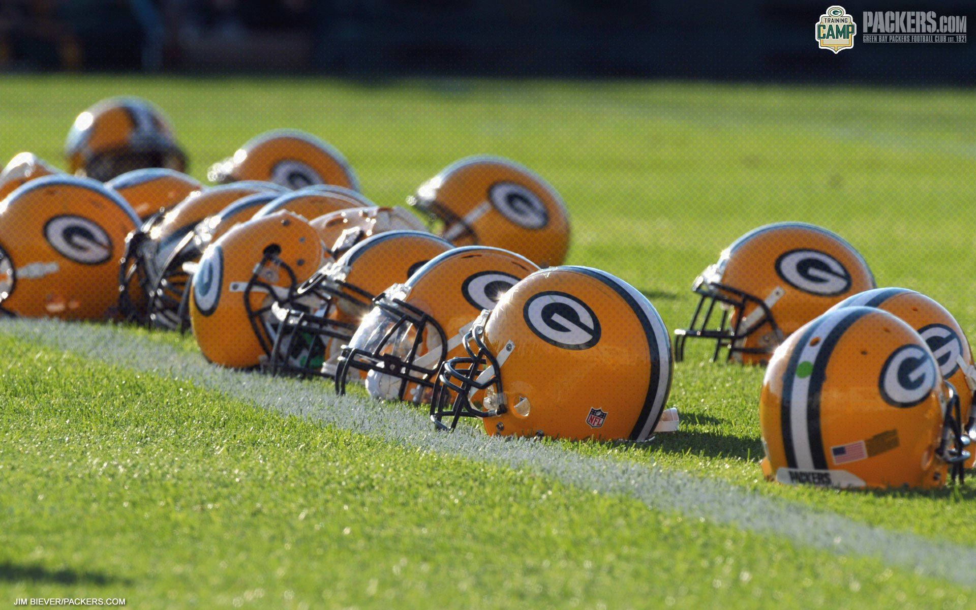 Packers 桌布 壁紙 — 一排鮮橙色的Green Bay Packers美式足球頭盔在陽光下放在充滿活力的綠色草地上。