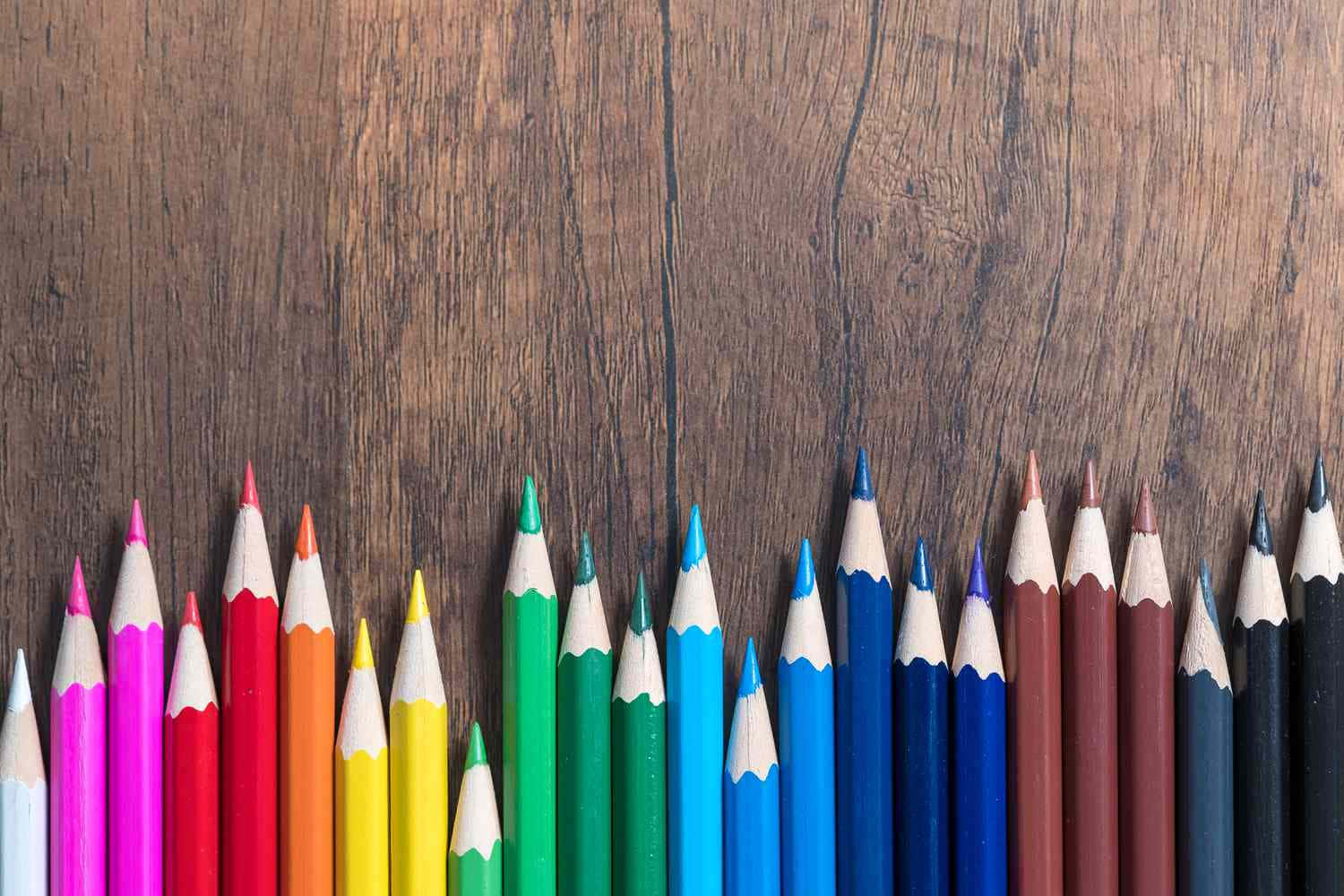 pencil 桌布 壁紙 — 一排鮮豔的削尖彩色鉛筆，按彩虹順序排列在質樸的木質表面上。
