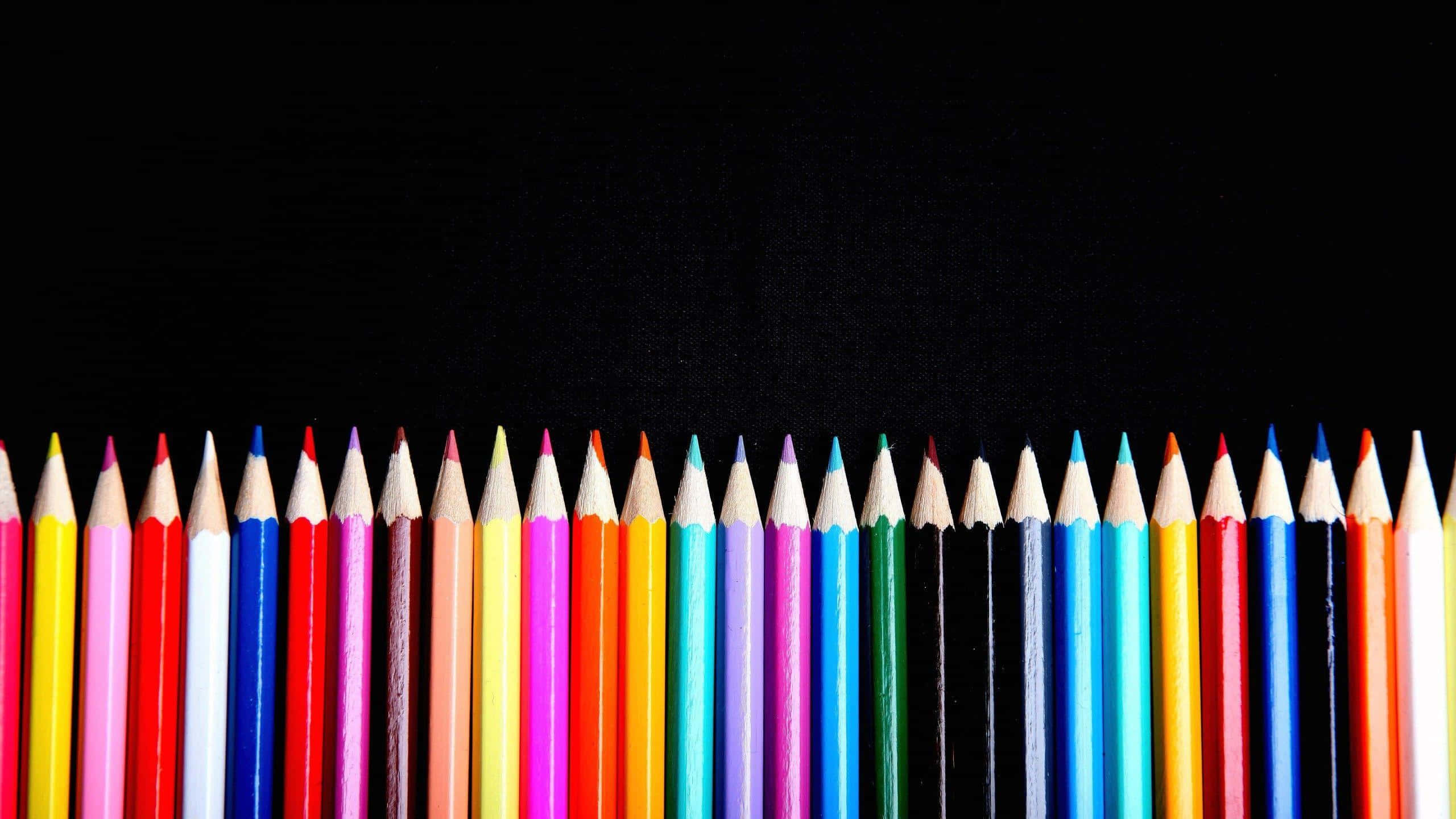 crayon 桌布 壁紙 — 一排鮮豔的削尖彩色鉛筆整齊地排列在純黑色背景前。