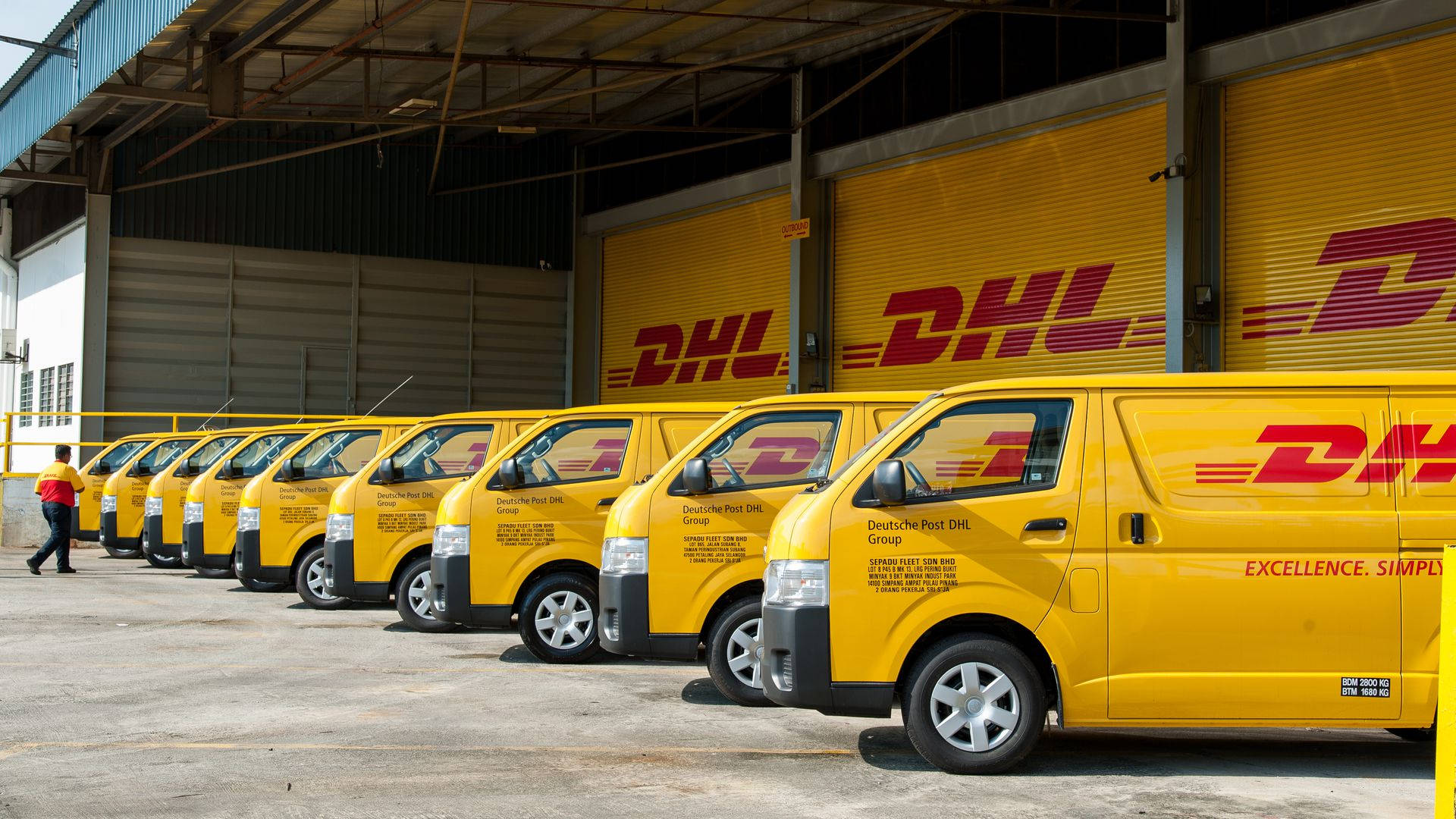 Dhl 桌布 壁紙 — 一排鮮黃色的DHL送貨貨車停放在一個有大型DHL品牌捲門的倉庫外面。