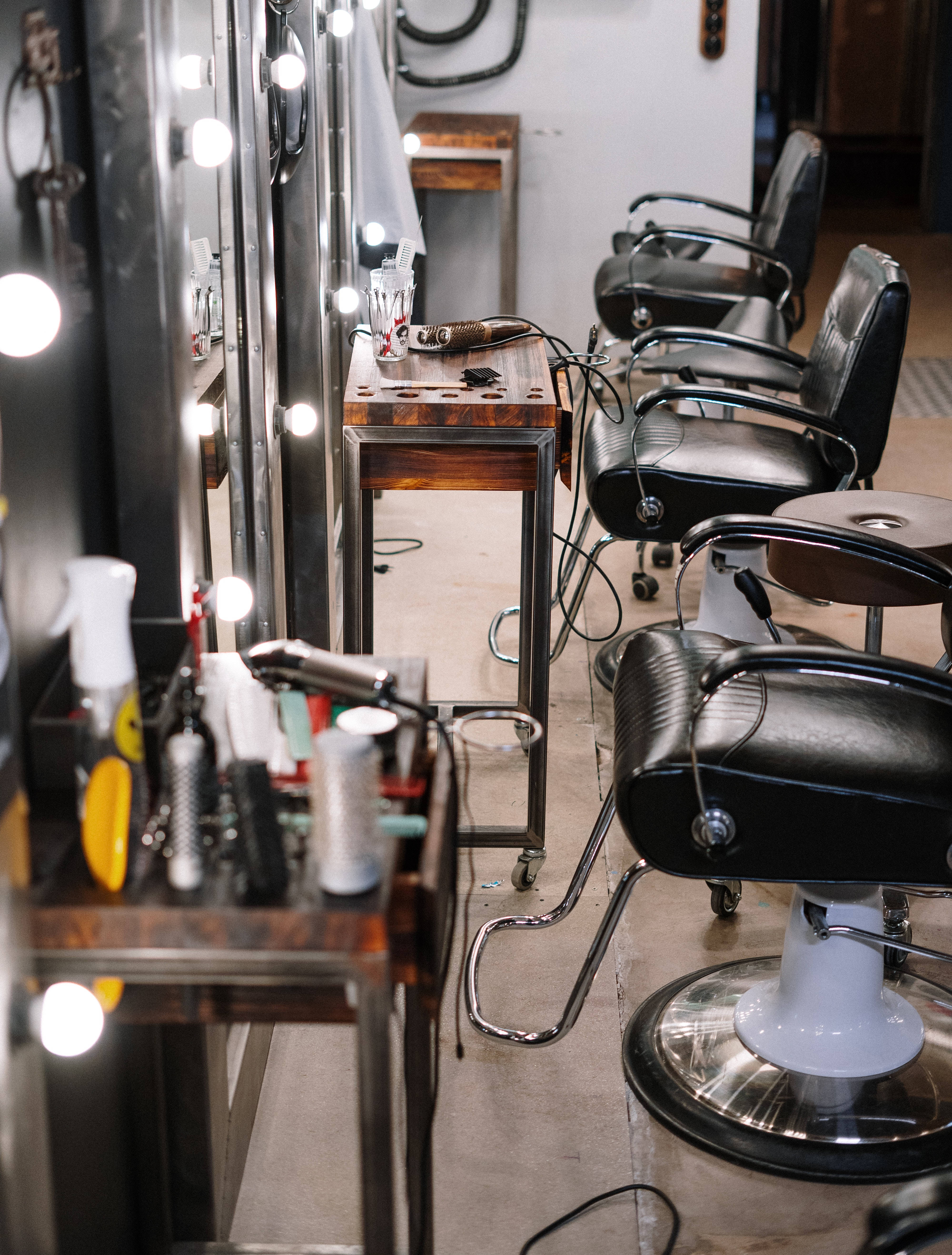 Salon 桌布 壁紙 — 一排黑色理髮椅配鍍鉻底座排列在復古理髮店中，由大鏡子周圍的明亮燈泡照亮。