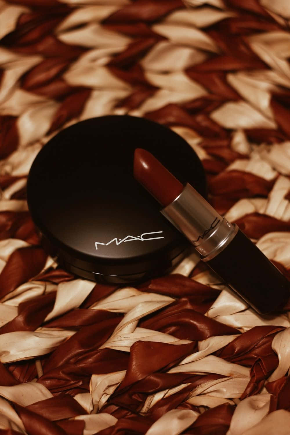 Mac Cosmetics 桌布 壁紙 — 一支MAC唇膏和粉餅放在豐富的棕色和奶油色編織布料上，帶有柔和溫暖的燈光。