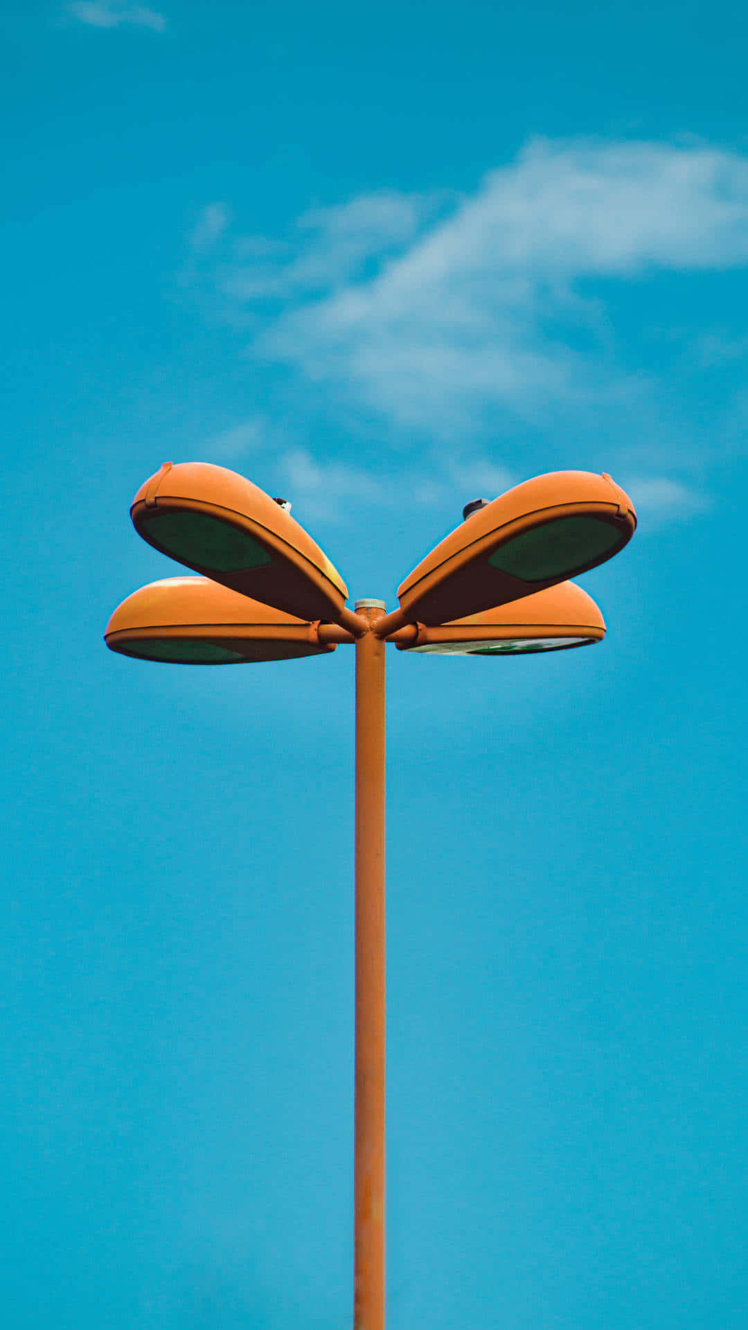 Street Light 桌布 壁紙 — 一支充滿活力的橙色路燈，帶有四盞彎曲的燈，高高聳立在清澈的藍天和縷縷白雲之間。
