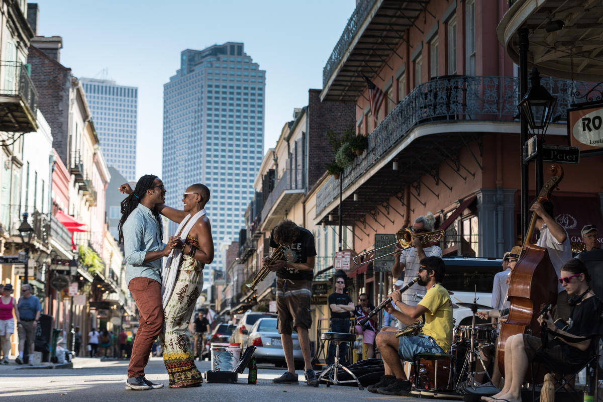 New Orleans 桌布 壁紙 — 一支充滿活力的街頭爵士樂隊在明媚陽光下表演，背景是歷史建築和現代摩天大樓。
