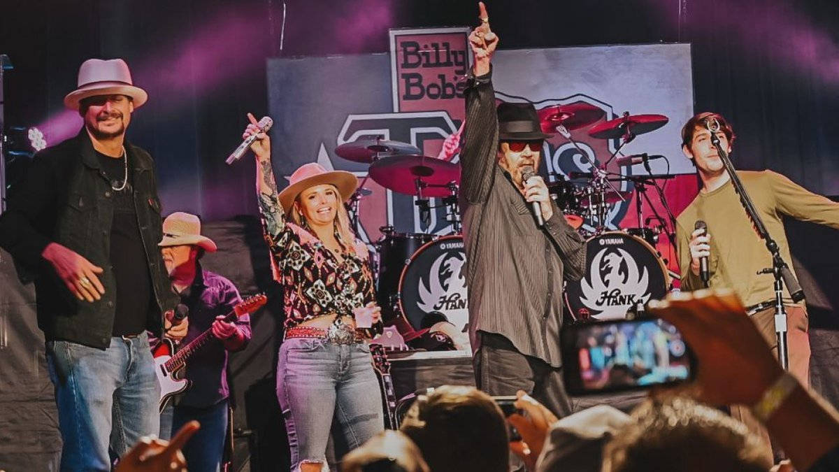 Worth 桌布 壁紙 — 一支充滿活力的鄉村樂團在Billy Bob's Texas的舞台上表演，粉絲們歡呼並用手機捕捉這一刻。