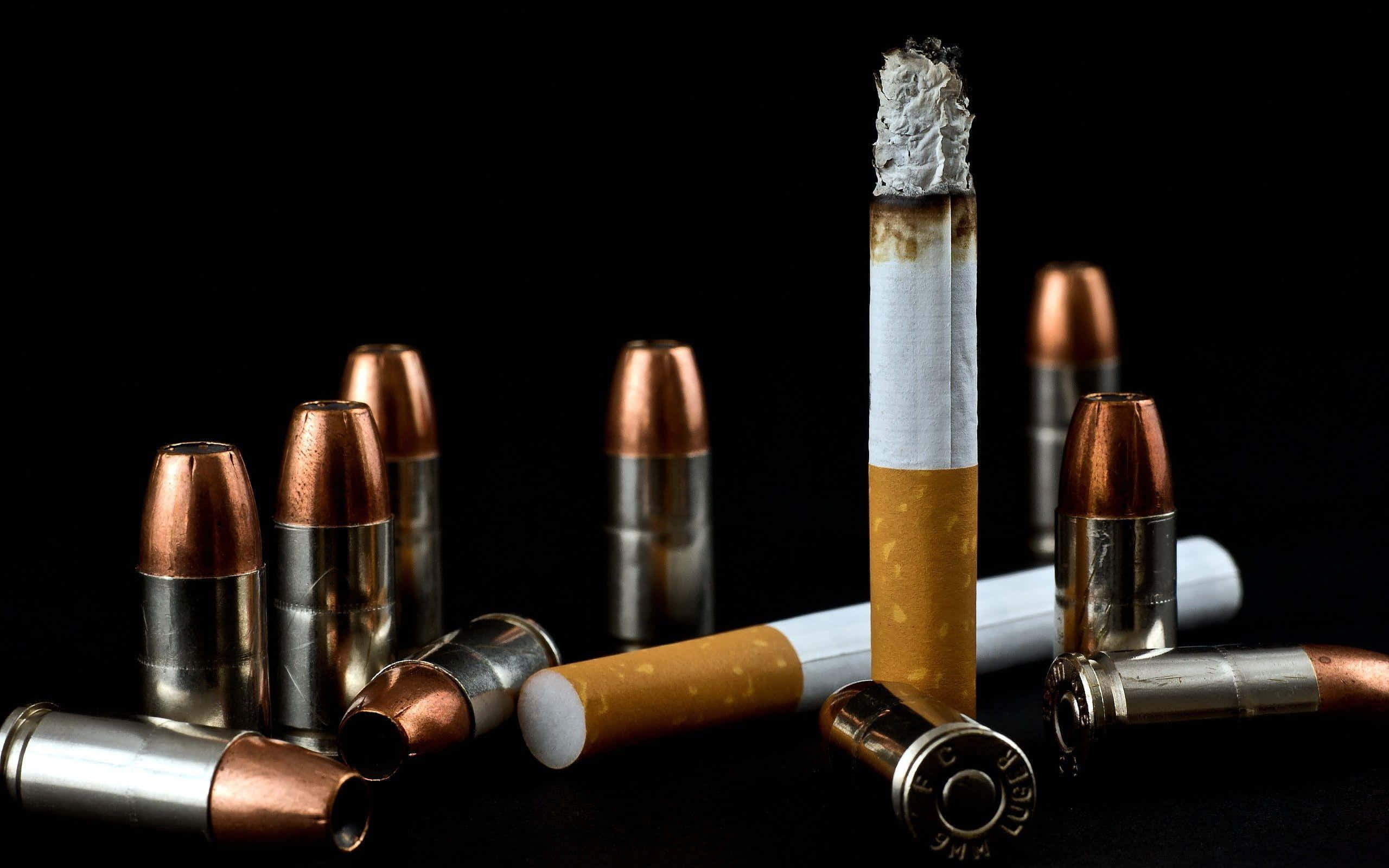 cigarettes 桌布 壁紙 — 一支冒煙的香煙在黑色背景下豎立於散落的子彈和折斷的煙蒂之間。