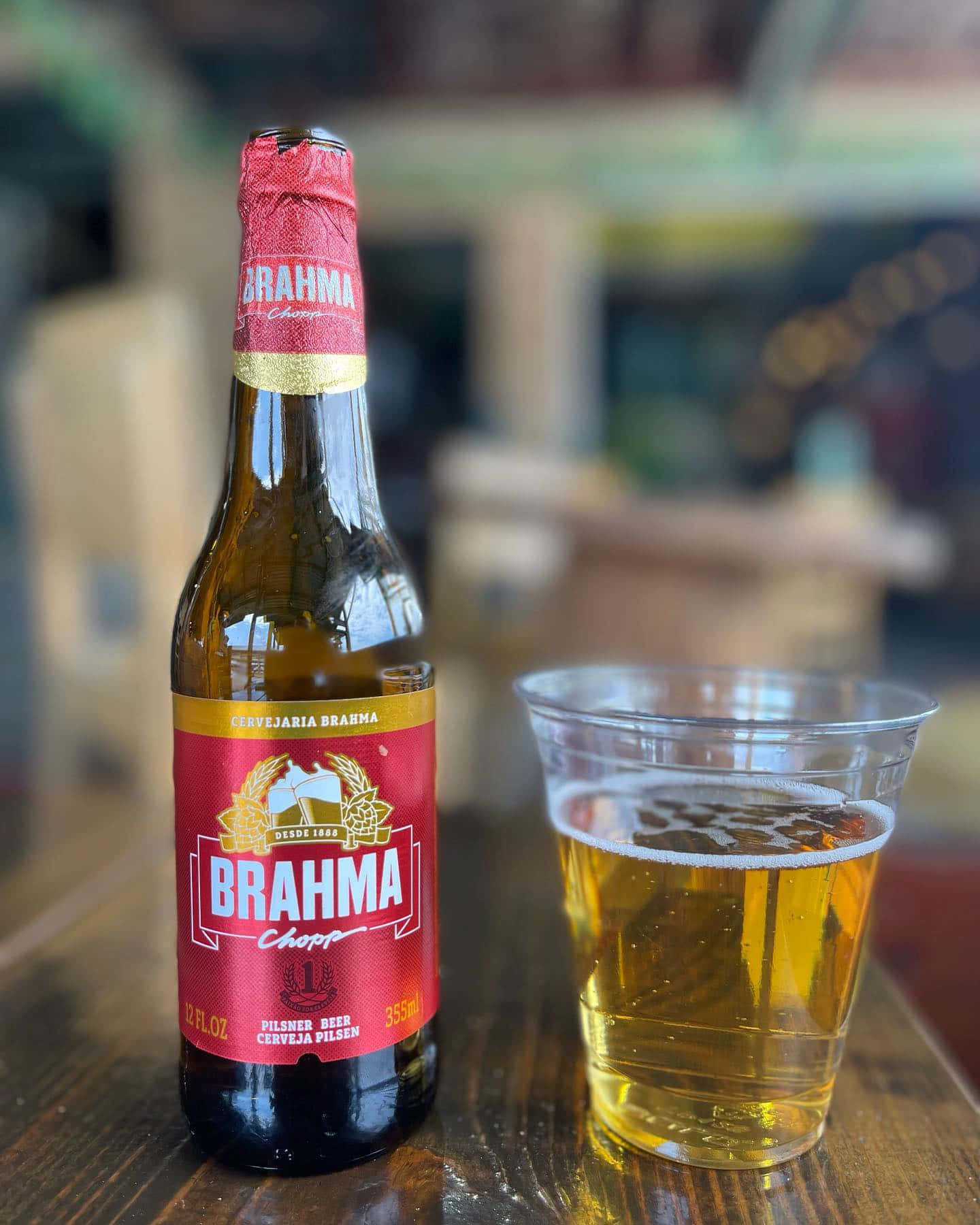 alcohol 桌布 壁紙 — 一支冰涼的Brahma啤酒瓶和一個裝滿的塑膠杯放在舒適酒吧的木桌上。