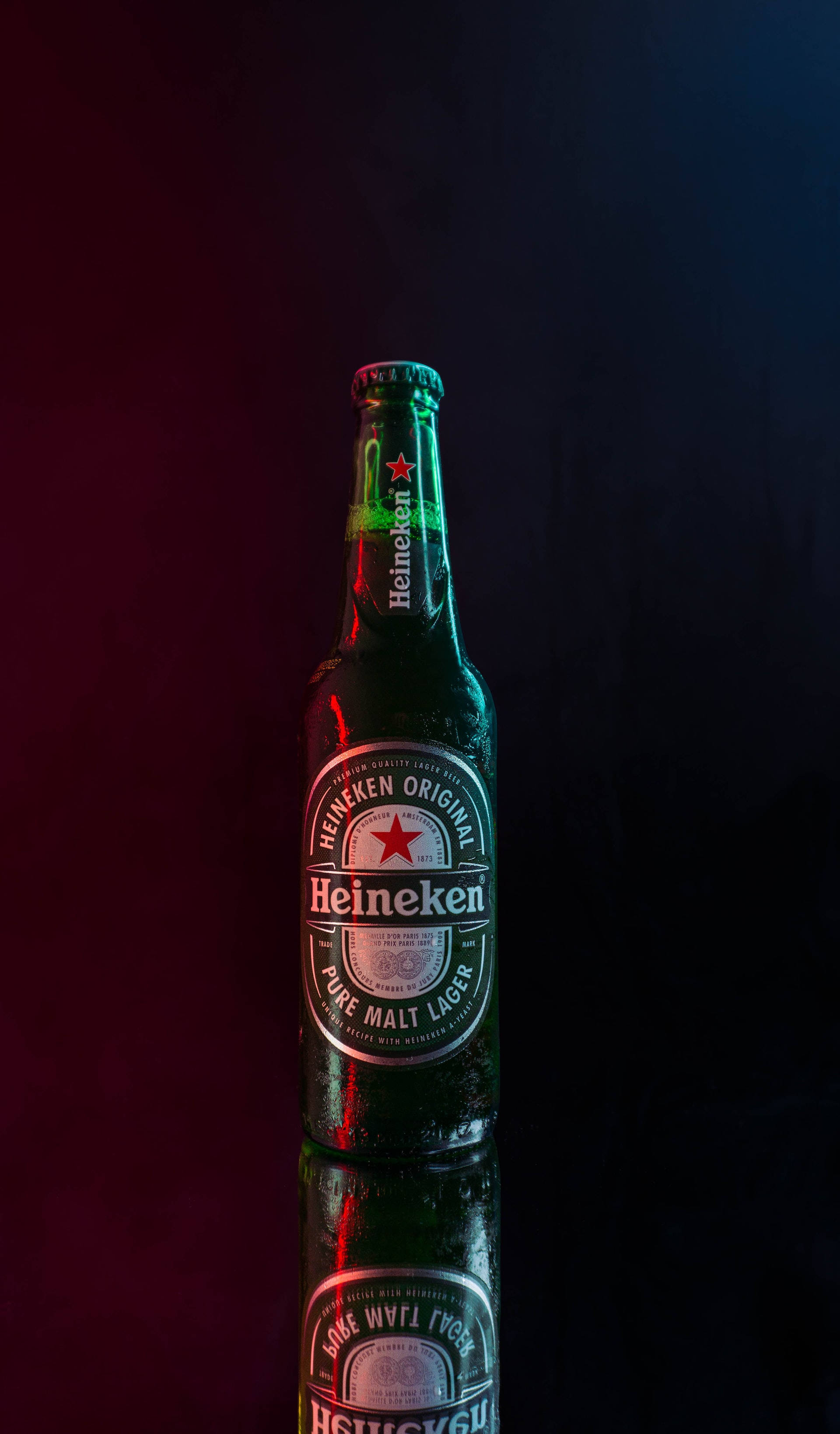 Drink 桌布 壁紙 — 一支冰涼的喜力啤酒瓶在深色背景下，於戲劇性的紅藍燈光照射下豎立在反光表面上。