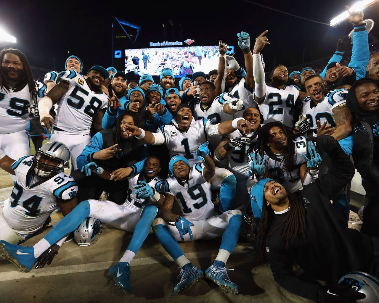 Panthers 桌布 壁紙 — 一支喜悅的卡羅萊納黑豹美式足球隊在夜間球場上高舉雙臂，帶著歡樂的表情慶祝勝利。