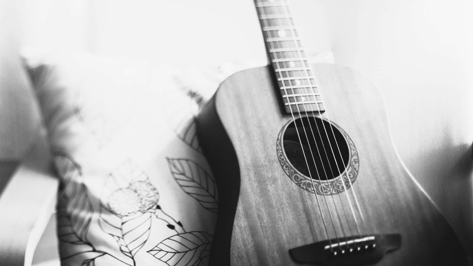 Black And White Guitar 桌布 壁紙 — 一支單色原聲吉他靠在有圖案的枕頭上，光線柔和擴散。