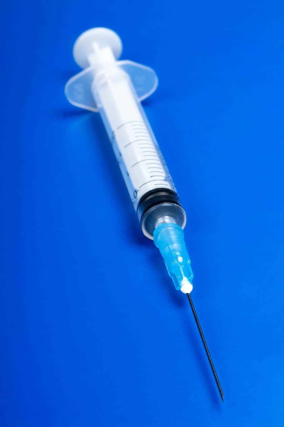 Vaccine 桌布 壁紙 — 一支帶有尖銳針頭的透明醫療注射器，對角線放置在鮮豔的藍色背景上。
