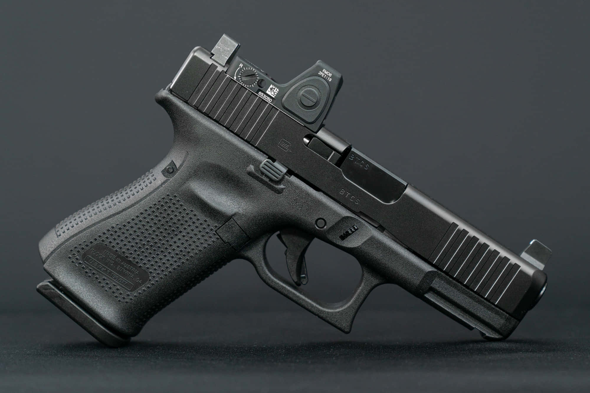 Glock 19 桌布 壁紙 — 一支帶有紅點瞄準器的時尚黑色Glock手槍，在攝影棚燈光下放置於深色表面上。