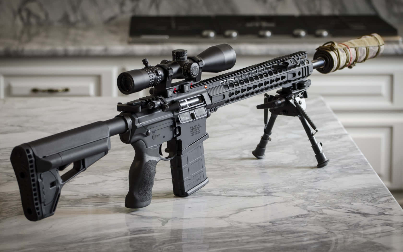 Rifle 桌布 壁紙 — 一支帶瞄準鏡和兩腳架的黑色戰術步槍放在大理石廚房檯面上，背景有爐灶。
