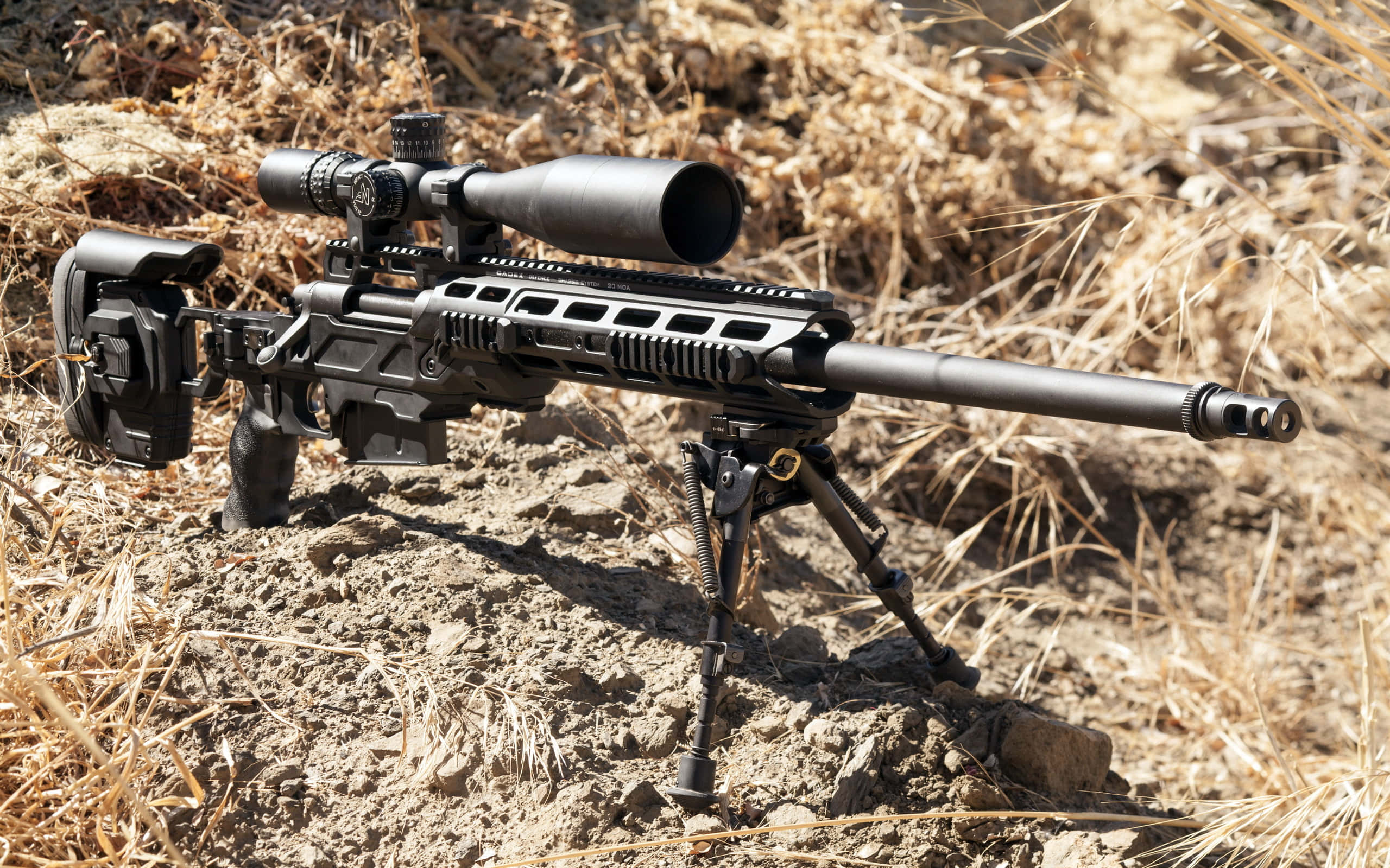 Rifle 桌布 壁紙 — 一支帶瞄準鏡和兩腳架的黑色戰術狙擊步槍，在明亮的陽光下擱在乾草和泥土上。