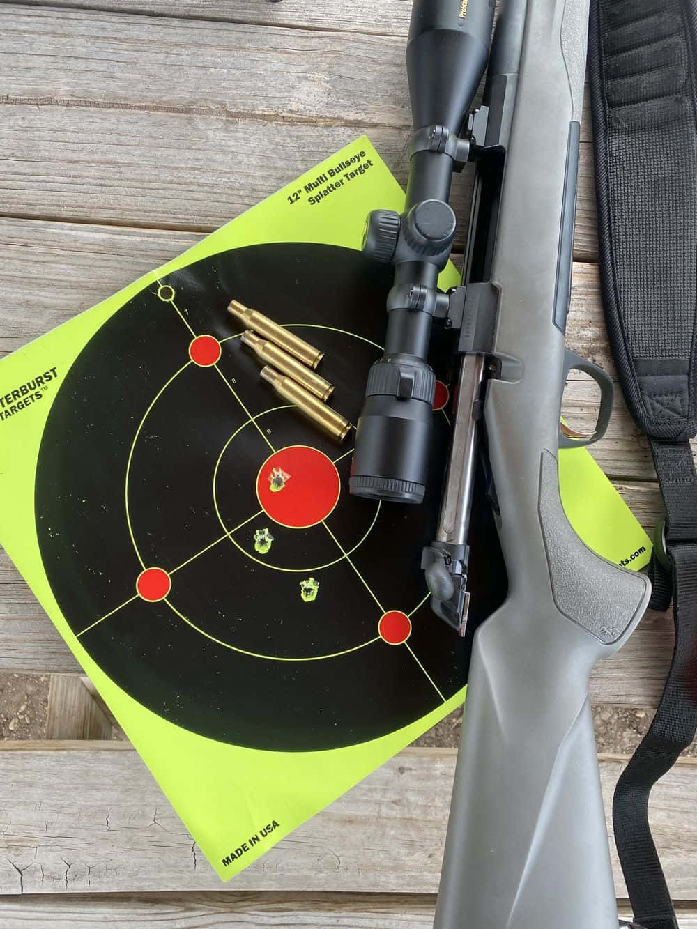 Shooting 桌布 壁紙 — 一支帶瞄準鏡的灰色步槍放在一個明亮的綠色靶心上，靶心上有彈孔和黃銅彈殼，置於風化的木板上。