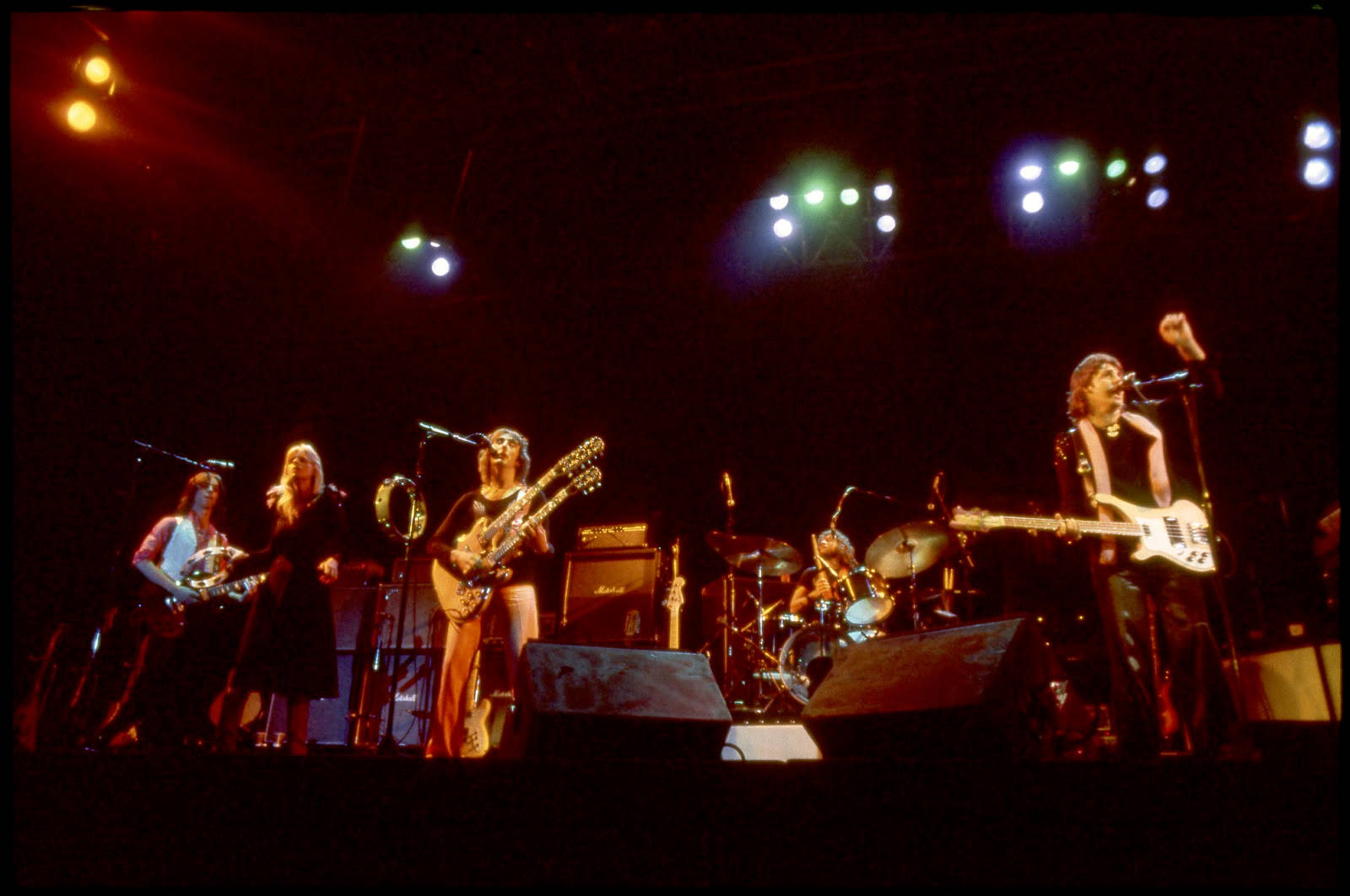 岩石 桌布 壁紙 — 一支復古搖滾樂團在昏暗的舞台上，在彩色聚光燈下，用吉他、鼓和麥克風表演。