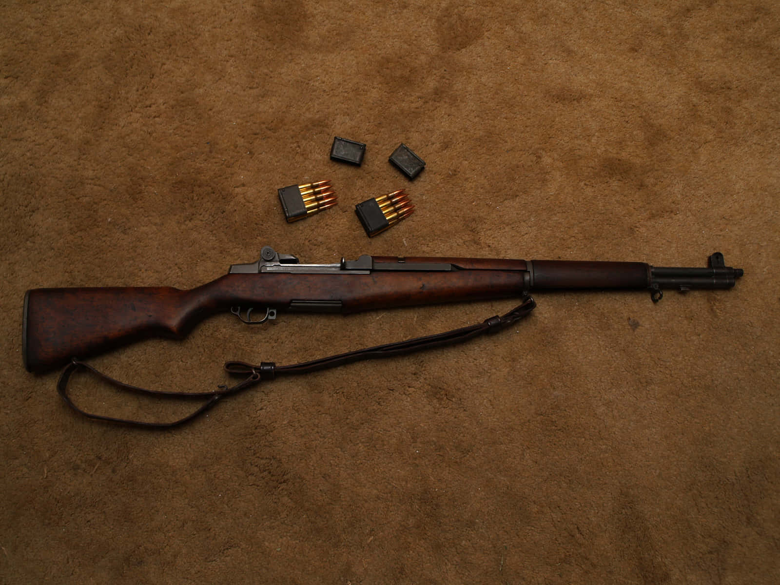 Rifle 桌布 壁紙 — 一支復古木製槍托步槍，配有皮革背帶和鬆散的子彈夾，放置在帶紋理的棕色表面上。