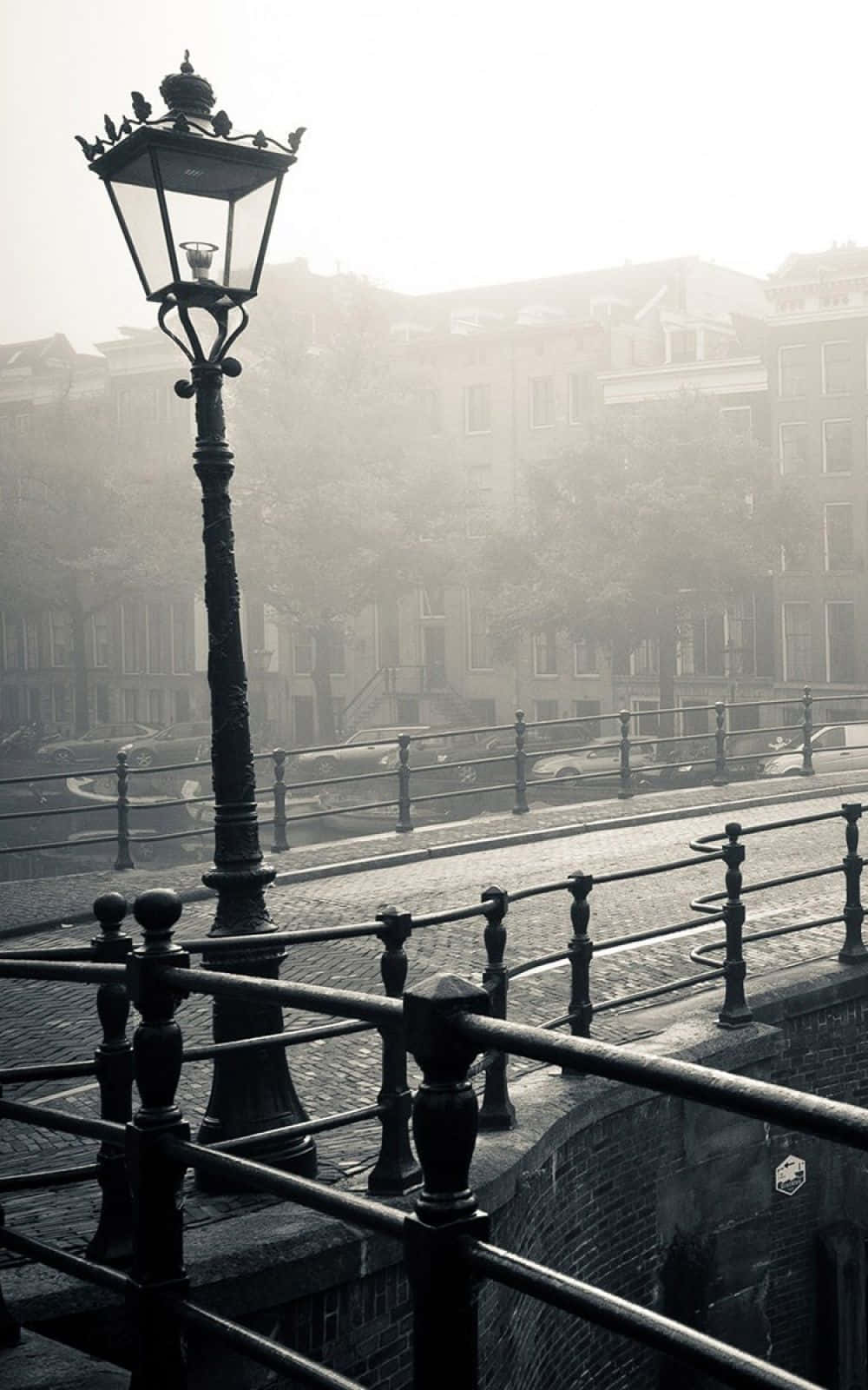 Black And White Street 桌布 壁紙 — 一支復古路燈矗立在霧氣瀰漫的橋上，俯瞰著霧濛濛的運河，背後是柔焦的歷史建築。