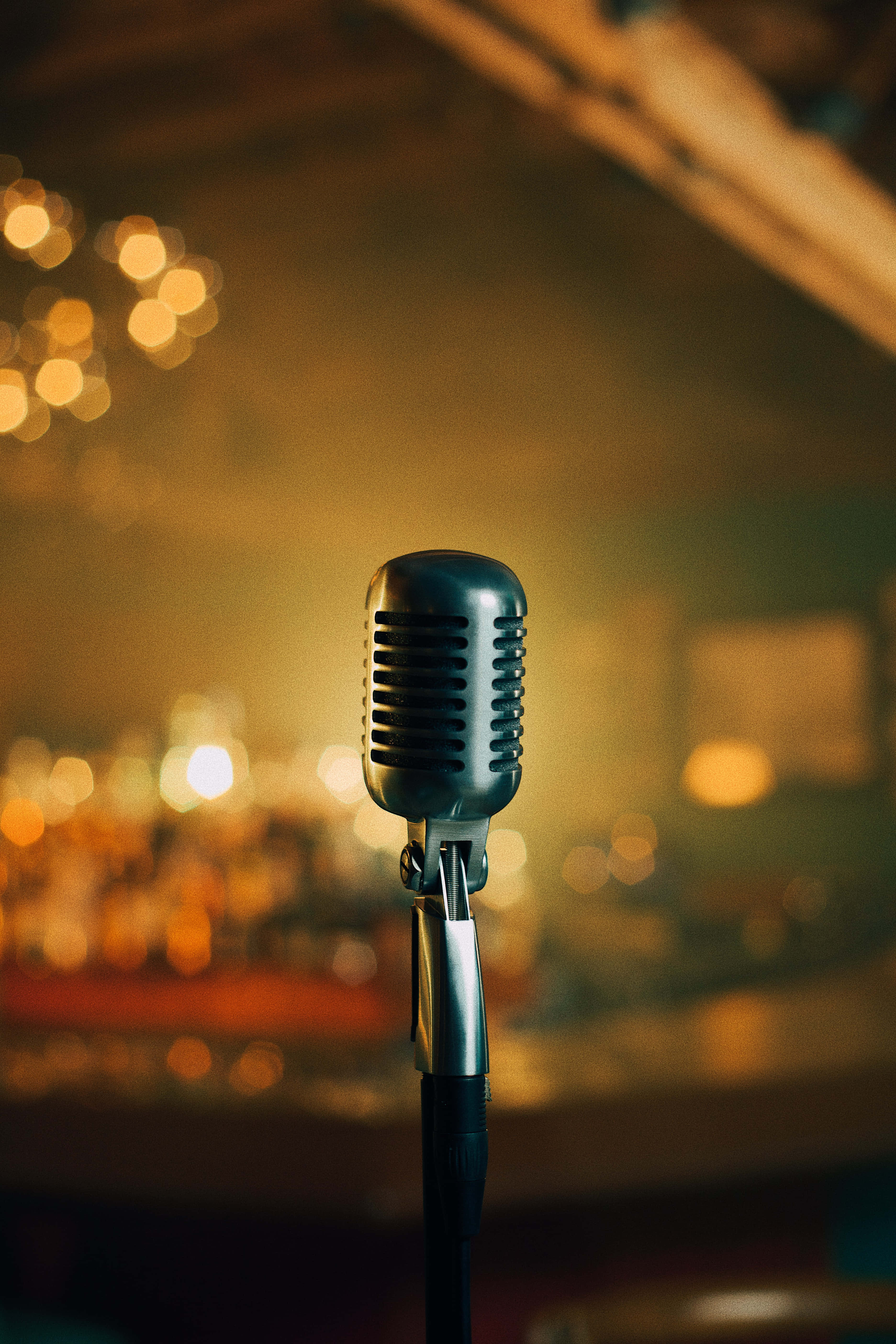 Microphone 桌布 壁紙 — 一支復古銀色麥克風豎立在支架上，背景是溫暖燈光下模糊的酒吧，帶有金色散景燈光。