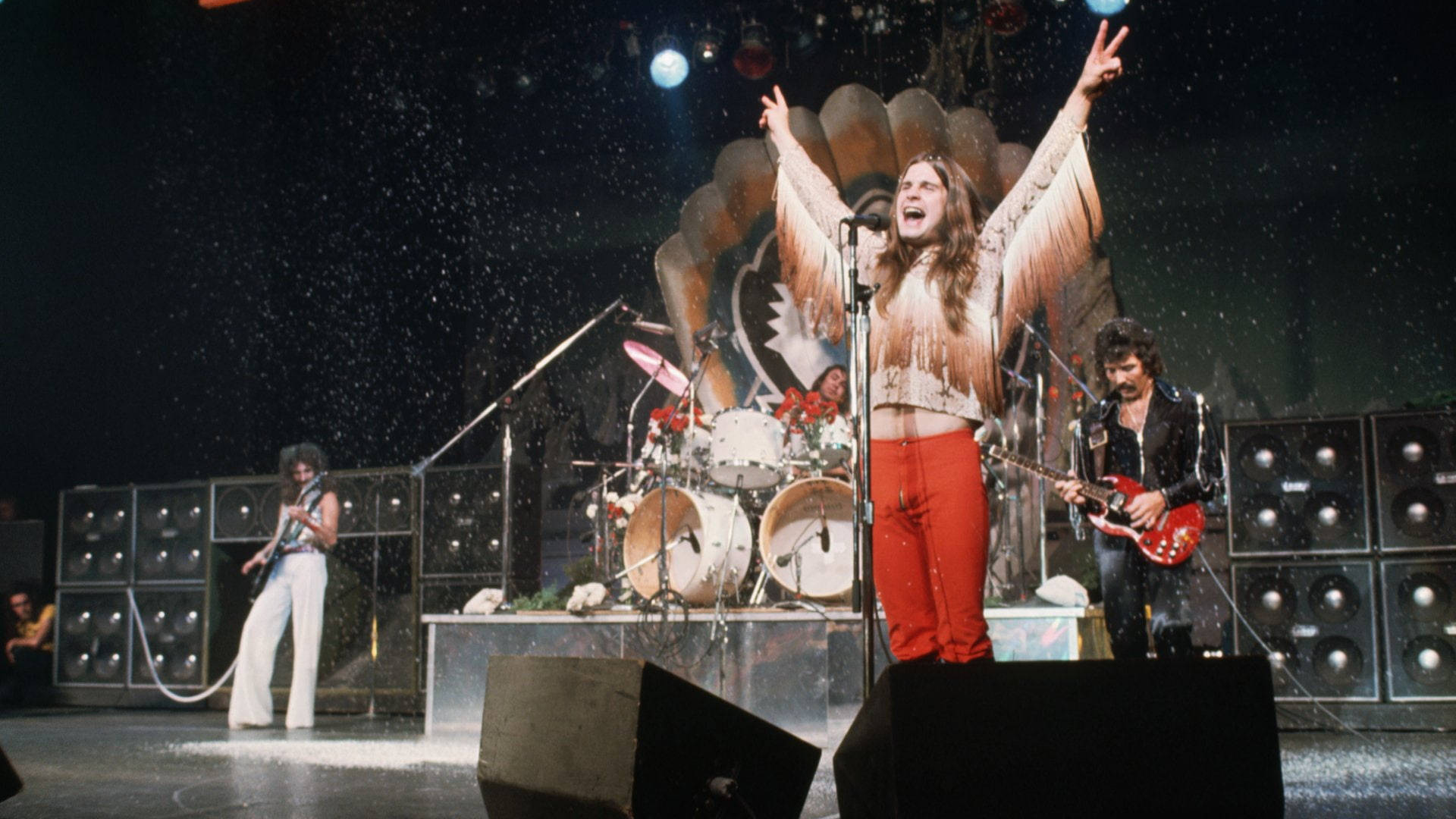 Ozzy Osbourne 桌布 壁紙 — 一支搖滾樂隊在明亮的燈光下充滿活力地表演，周圍有五彩紙屑飄落。