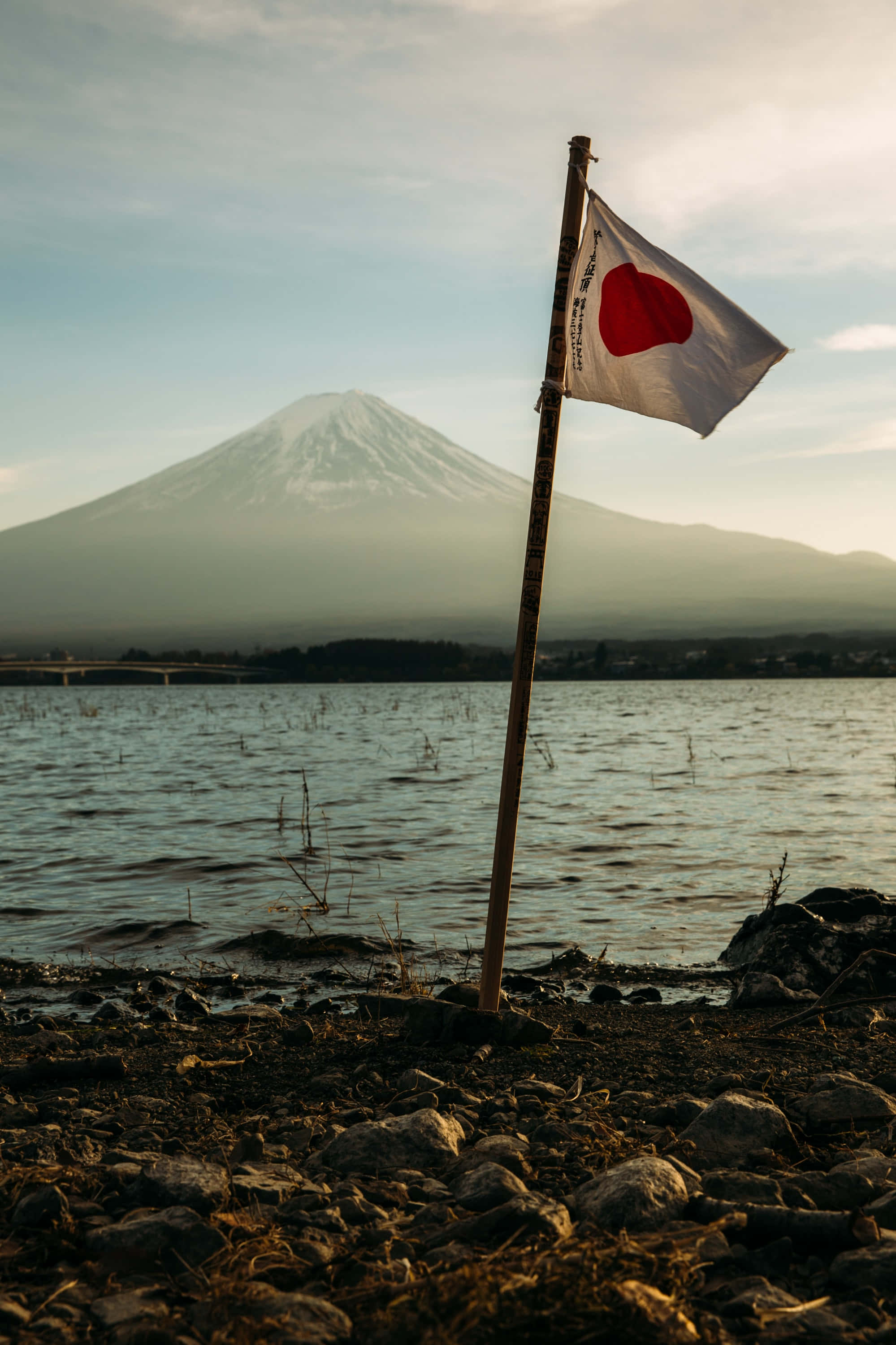 桌布 壁紙 — 一支日本國旗在湖岸的棍子上飄揚，背景是夕陽下積雪的富士山。