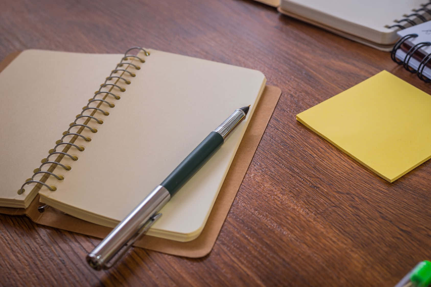 Notebook 桌布 壁紙 — 一支時尚的筆放在打開的螺旋筆記本上，旁邊是溫暖的木桌上的一張黃色便利貼。