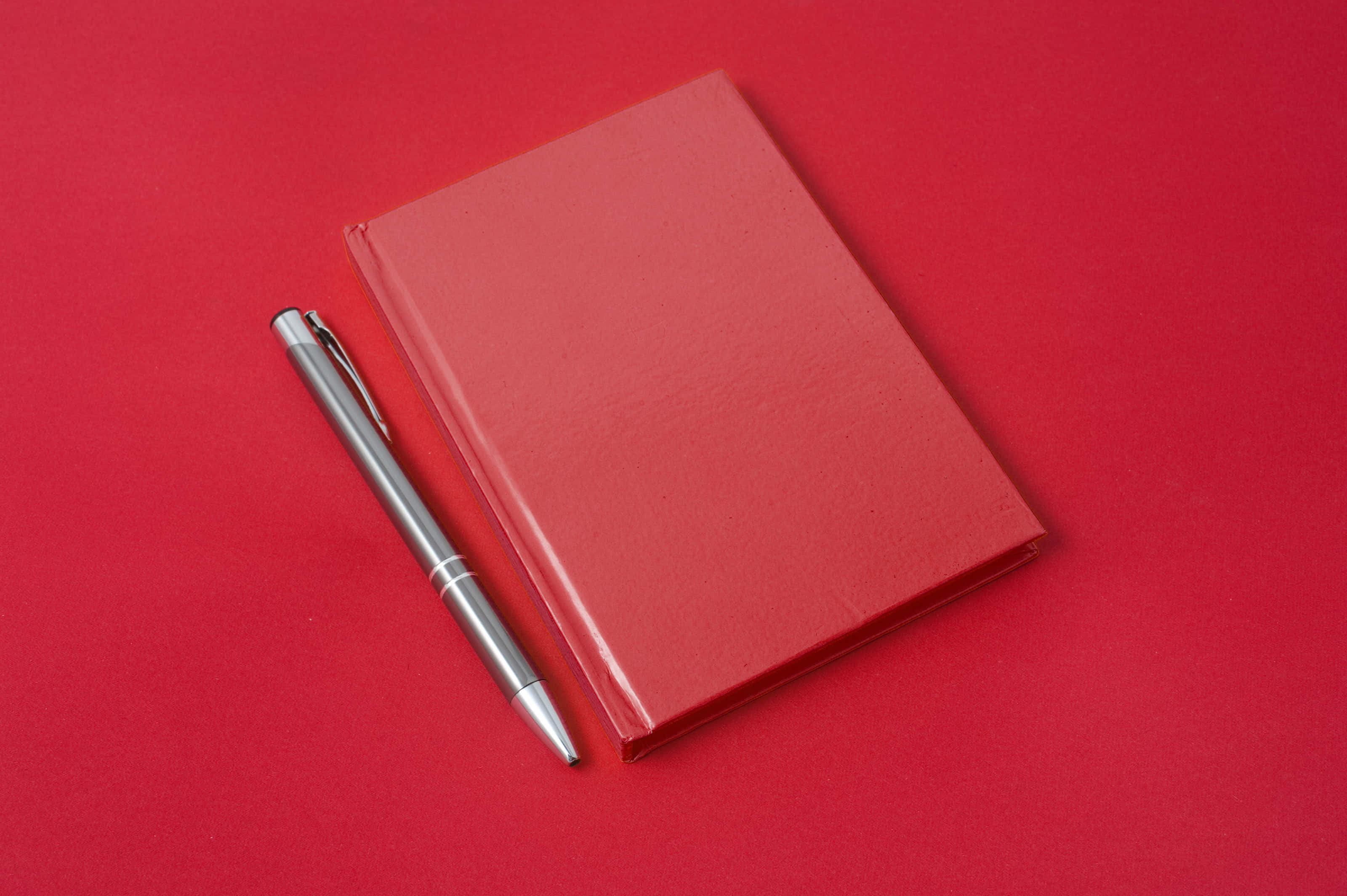 Diary 桌布 壁紙 — 一支時尚的銀色筆放在一張鮮紅色的表面上，旁邊是一本有紋理的紅色筆記本。