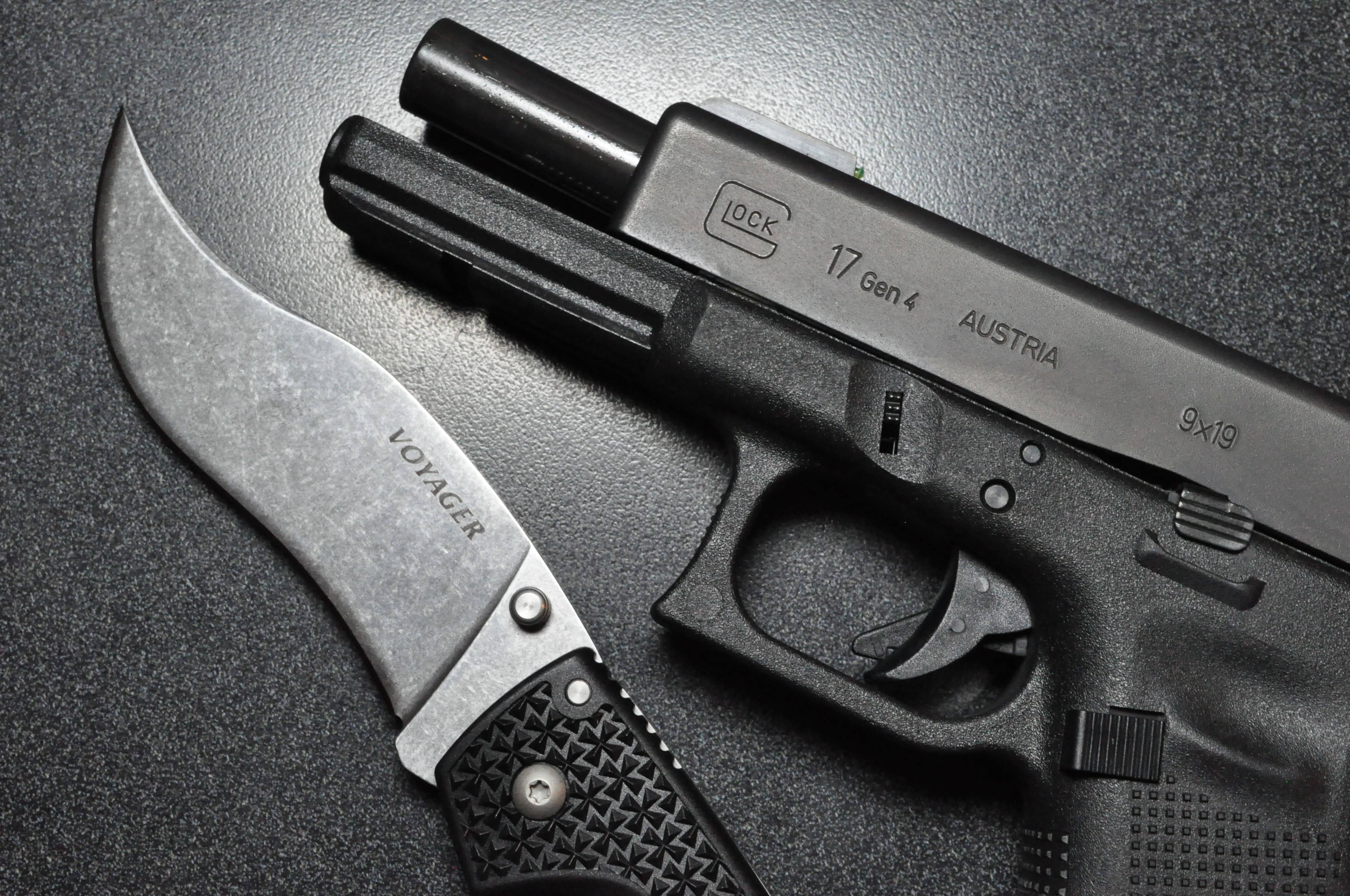 克拉克 桌布 壁紙 — 一支時尚的黑色Glock 17 Gen 4手槍和一把Voyager彎刀放在深色紋理表面上，在戲劇性的燈光下。