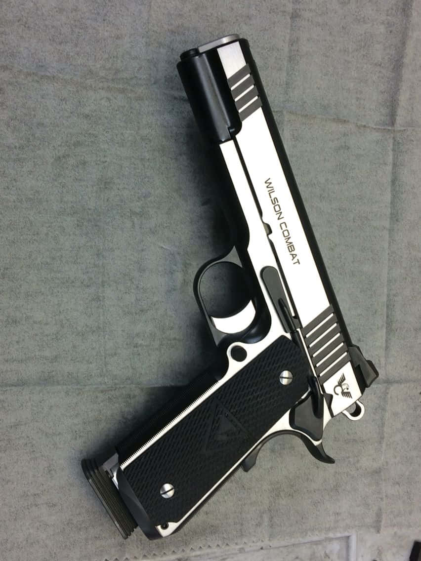 pistol 桌布 壁紙 — 一支時尚的黑色和銀色 Wilson Combat 手槍斜放在有紋理的灰色布料表面上。