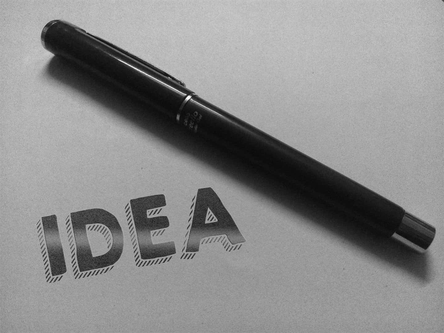 Pen 桌布 壁紙 — 一支時尚的黑色筆斜放在紙上，旁邊是粗體草書風格的「IDEA」字樣。