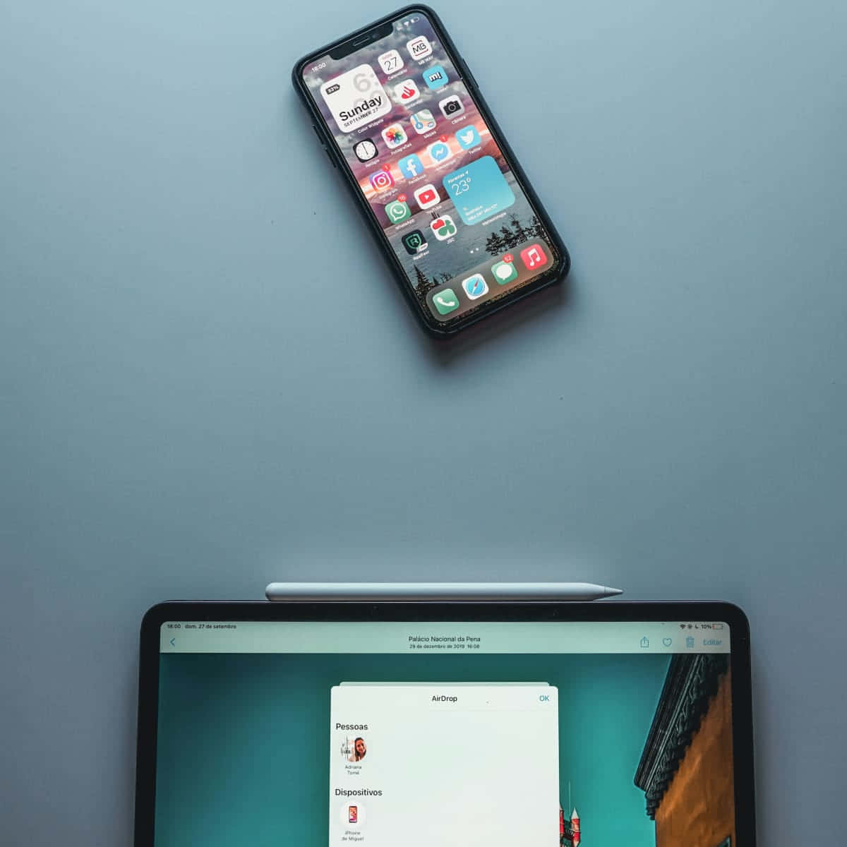 iPhone 桌布 壁紙 — 一支智慧型手機和一台筆記型電腦放在柔和的藍色表面上，螢幕上顯示AirDrop已啟用。