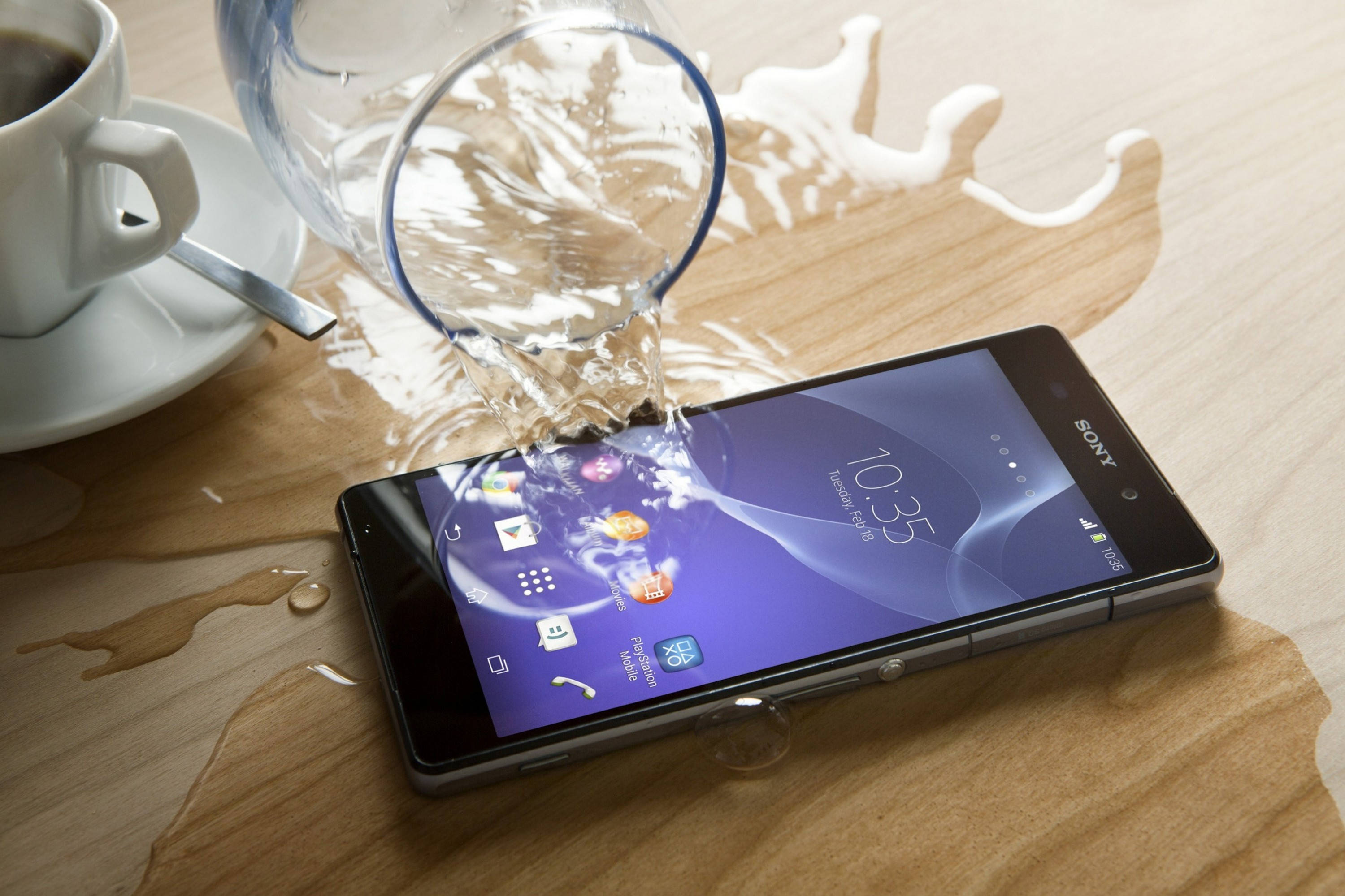 Sony 桌布 壁紙 — 一支智慧型手機放在木桌上，水從玻璃杯濺到螢幕上，旁邊有一杯咖啡。