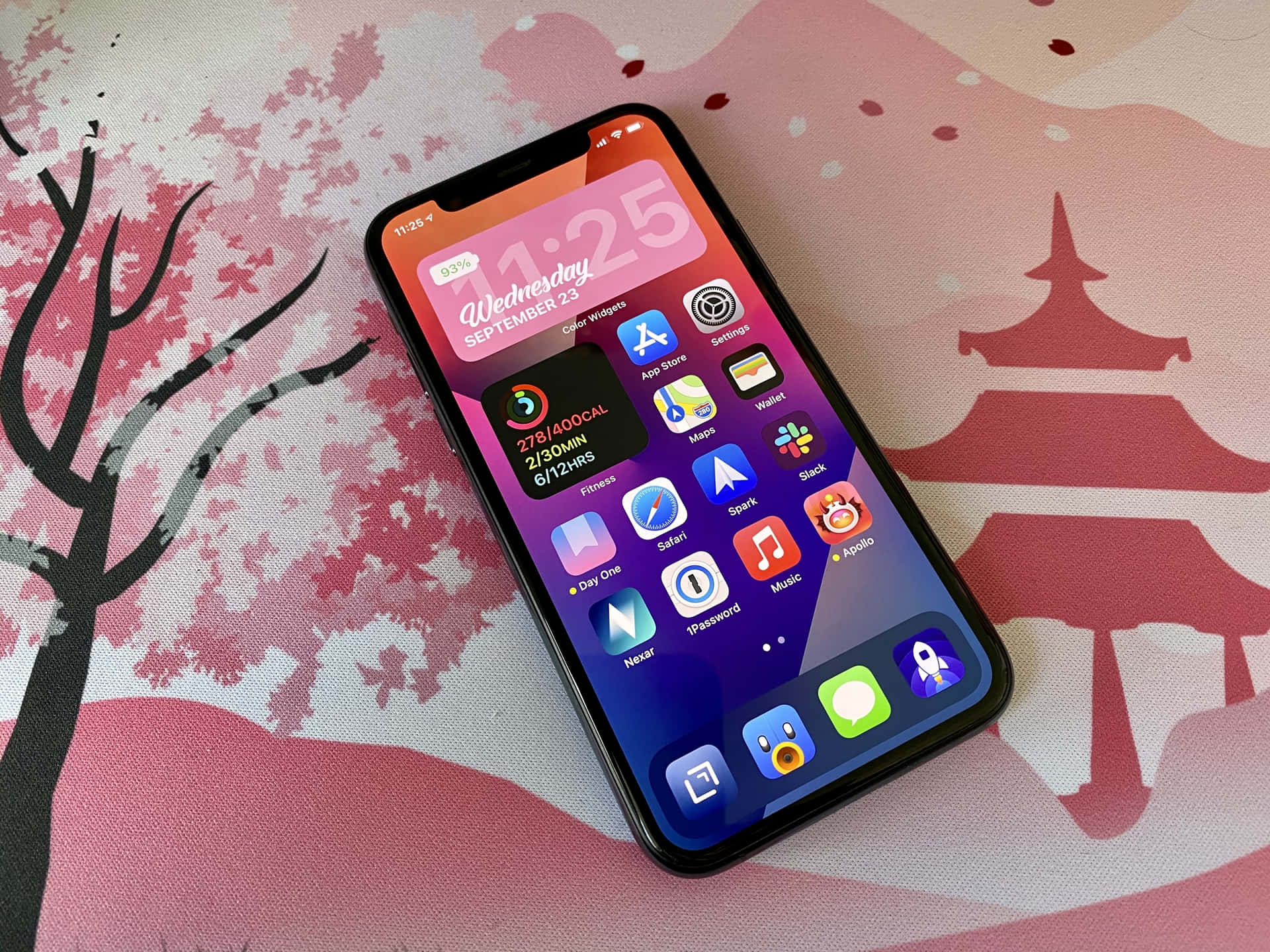 智慧型手機放在櫻花圖案表面，帶有寶塔和樹木設計。 — iPhone 14 壁紙