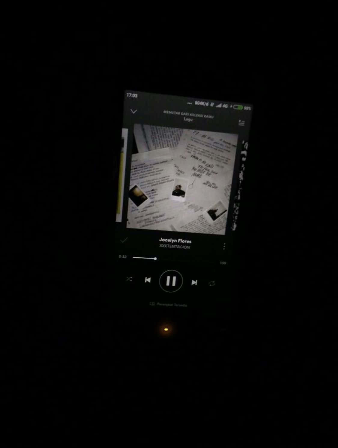 Aesthetic Grunge Phone 桌布 壁紙 — 一支智慧型手機螢幕在黑暗中發光，顯示一個音樂播放器，帶有黑白專輯封面，上面散佈著手寫筆記和照片。