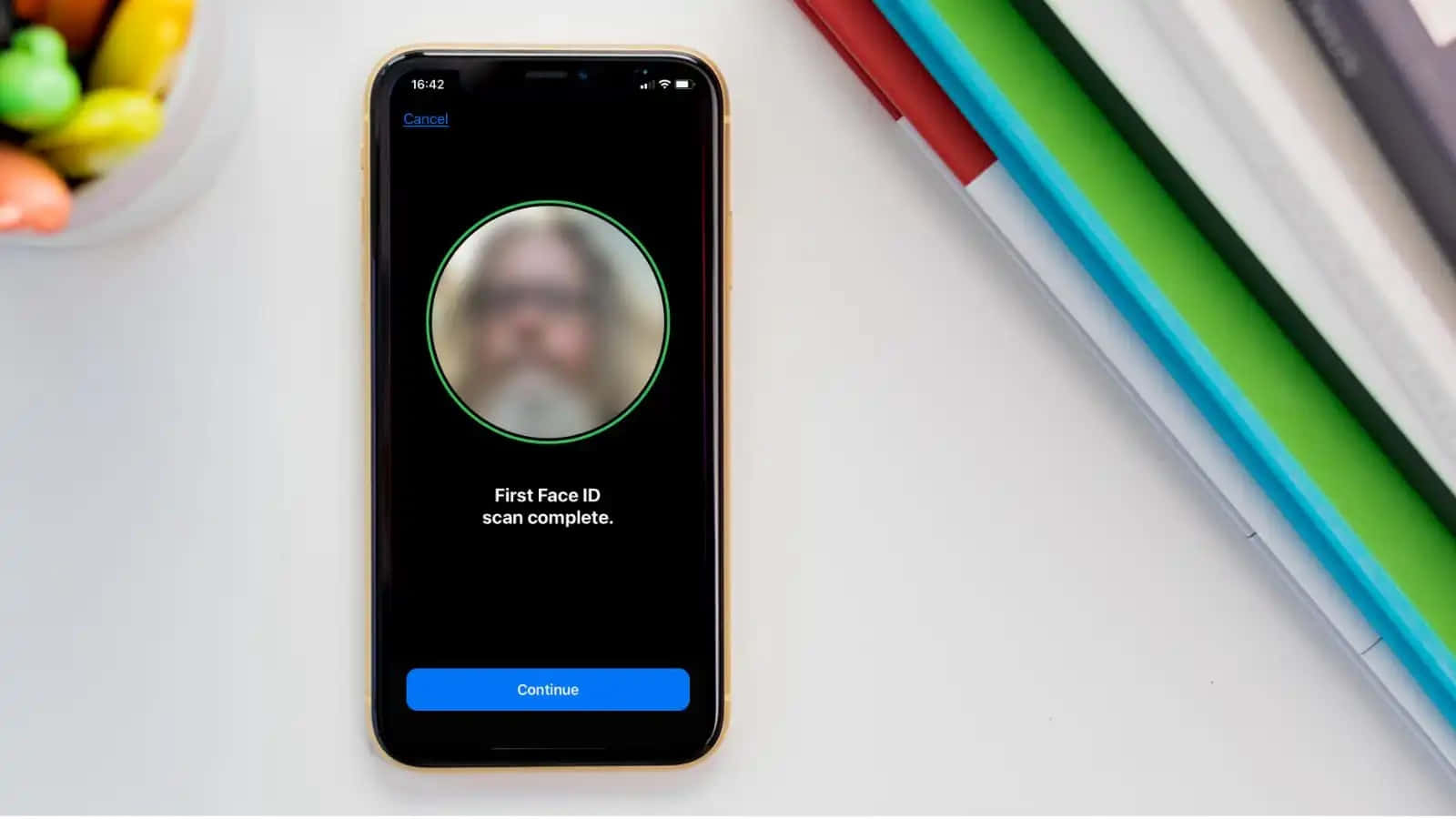 Face Id 桌布 壁紙 — 一支智慧型手機顯示已完成的 Face ID 掃描，附近有模糊的臉孔和彩色筆在白色桌子上。