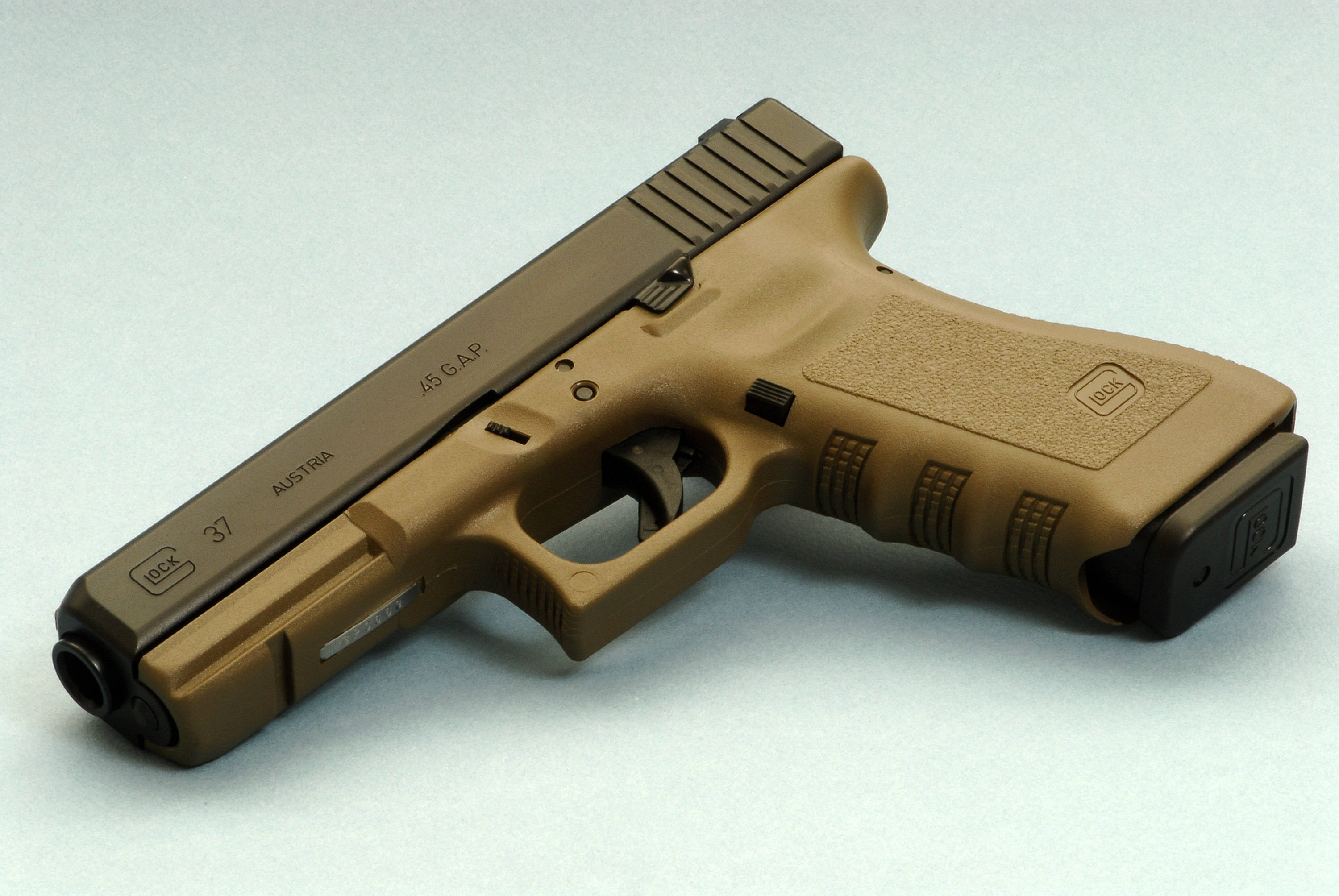 克拉克 桌布 壁紙 — 一支棕褐色和黑色的Glock 37手槍，帶有.45 GAP口徑標記，斜放在純淺灰色表面上。