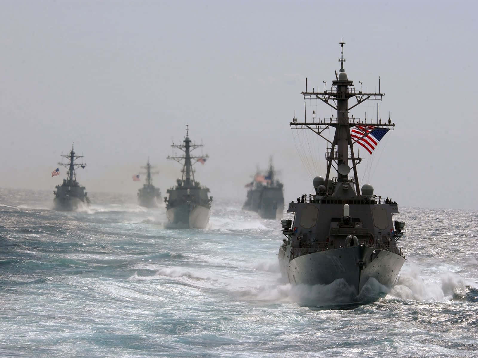 Navy 桌布 壁紙 — 一支灰色海軍軍艦艦隊在波濤洶湧的藍色海面上破浪前進，美國國旗迎風飄揚，以編隊行進。