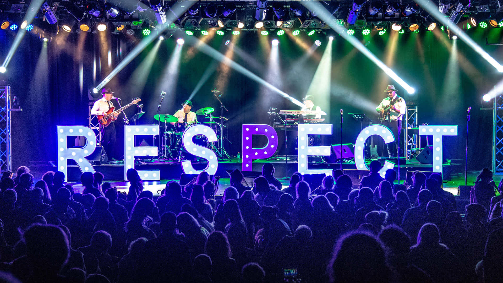 Respect 桌布 壁紙 — 一支現場樂隊在充滿活力的聚光燈下於舞台上表演，一個巨大的發光 'RESPECT' 標誌面向夜晚投入的觀眾。